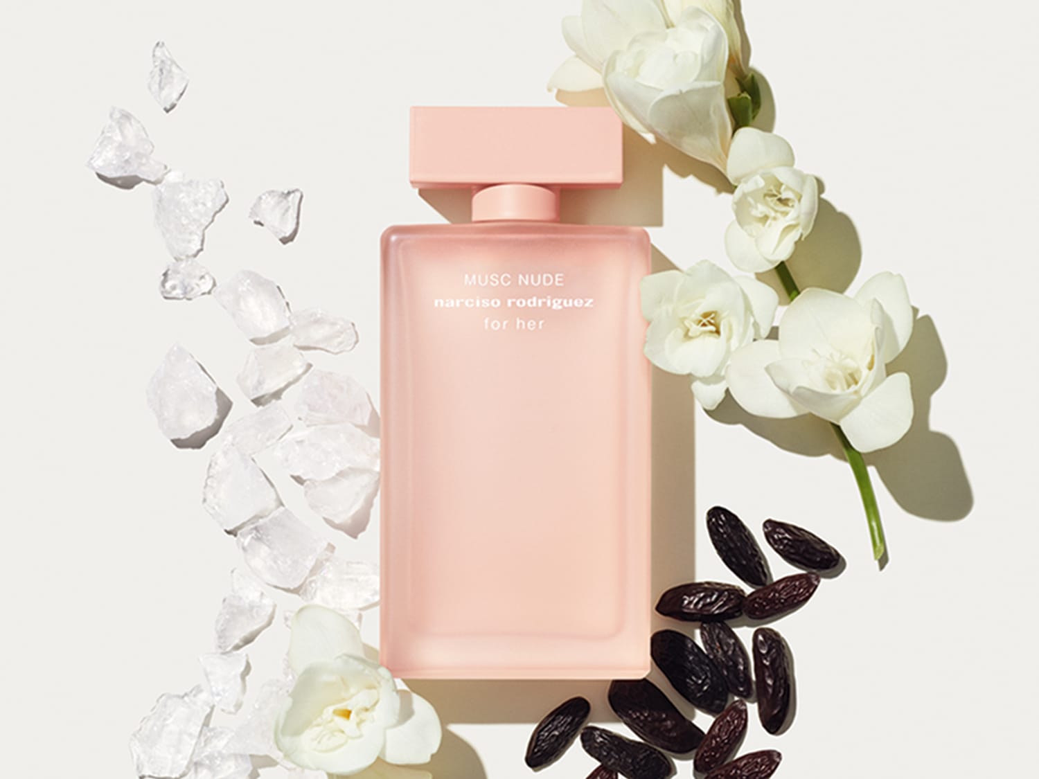 Ein zartrosa Flakon von Narciso Rodriguez 'Musc Nude for her' liegt inmitten von weißen Blüten, transparenten Kristallen und dunklen Samen.