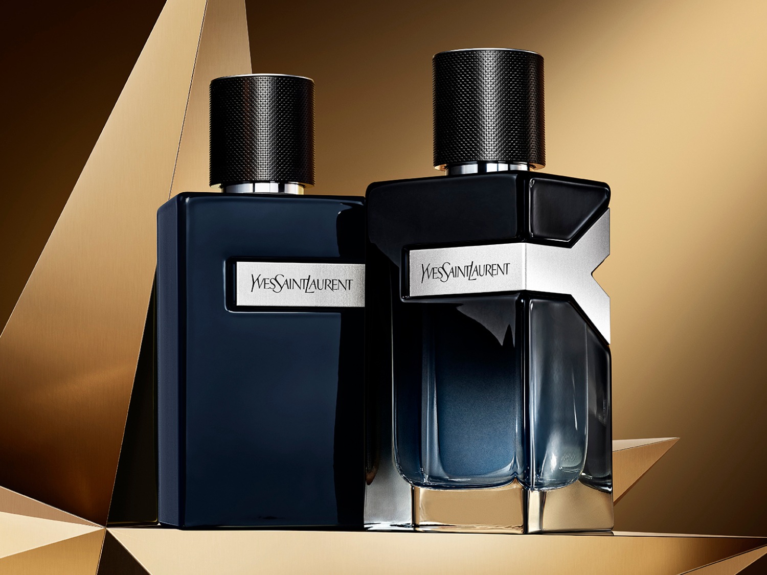 Twee flessen YSL-parfum, de ene donkerblauw en rechthoekig, de andere met een zilveren Y-vormig detail, staan op een gouden achtergrond.