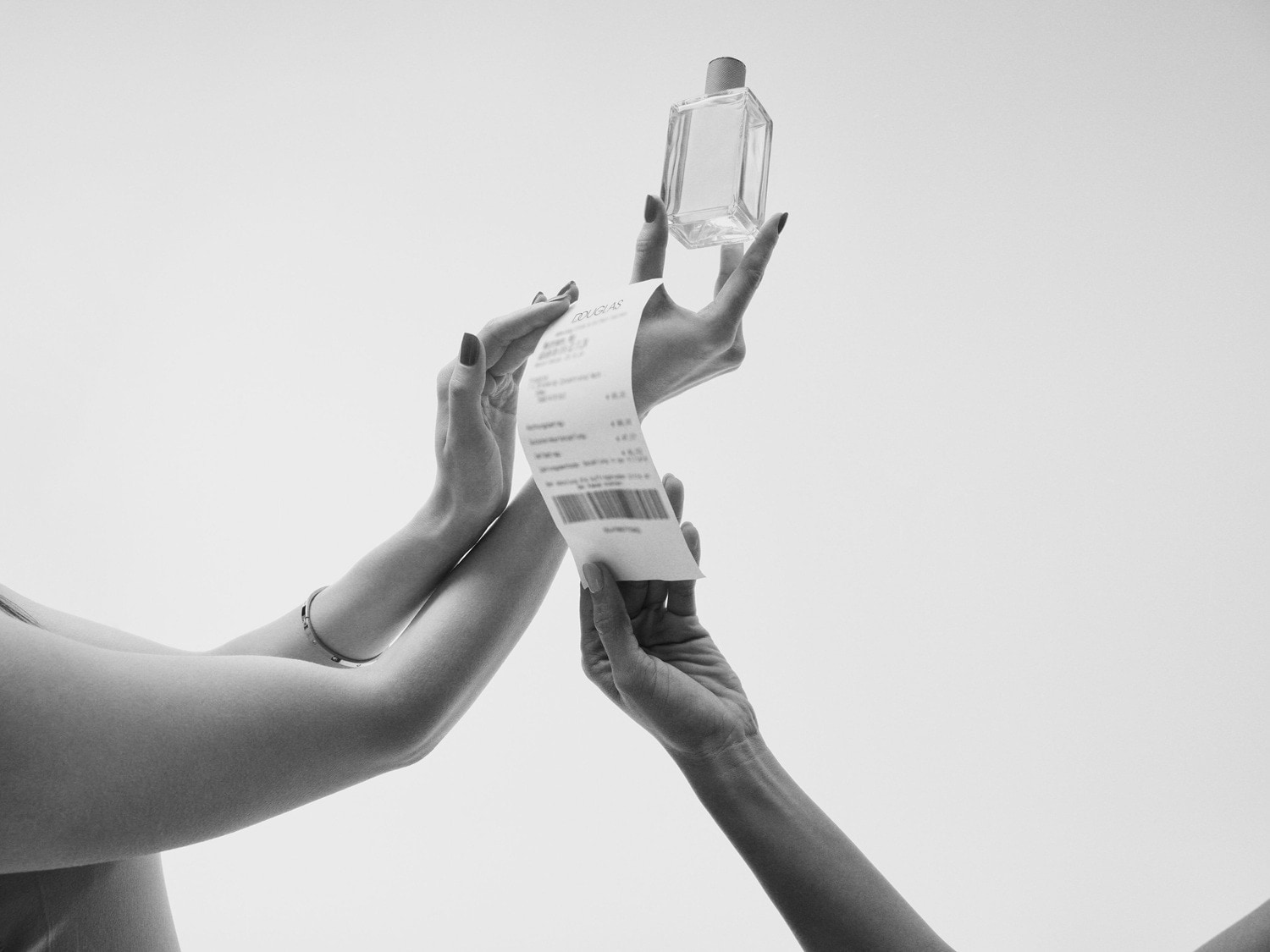 Two hands hold a Douglas receipt and a clear glass perfume bottle against a white background, showcasing a recent purchase.
