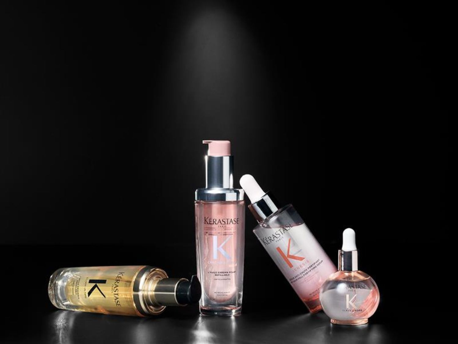 Čtyři lahvičky vlasových sér Kérastase v odstínech zlaté a růžové s kapátkem a pumpičkou na černém pozadí.