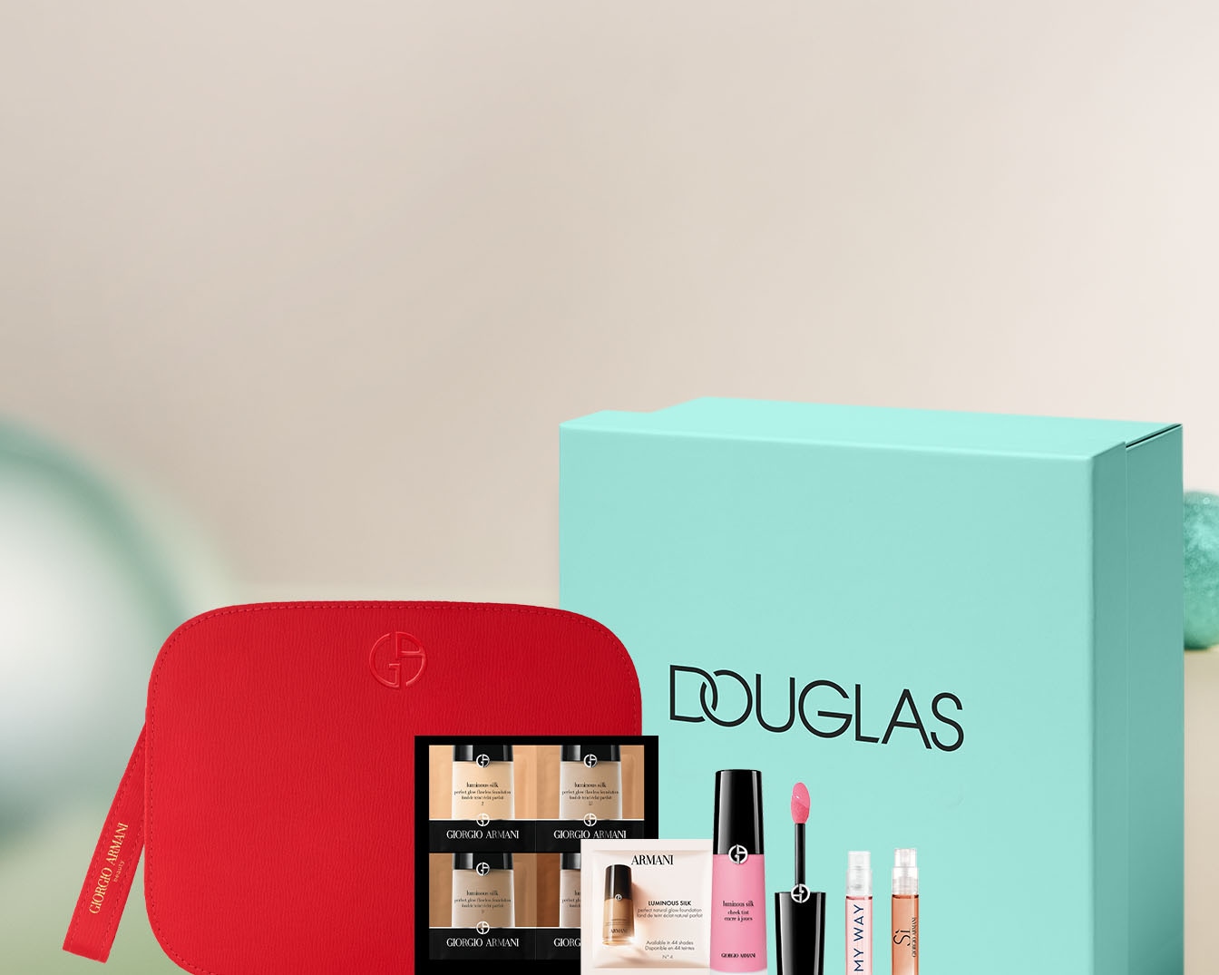 Zestaw upominkowy Giorgio Armani w czerwonej kosmetyczce z logo marki, obok pudełko Douglas z miniaturami kosmetyków, w tym podkładu Luminous Silk i perfum My Way.