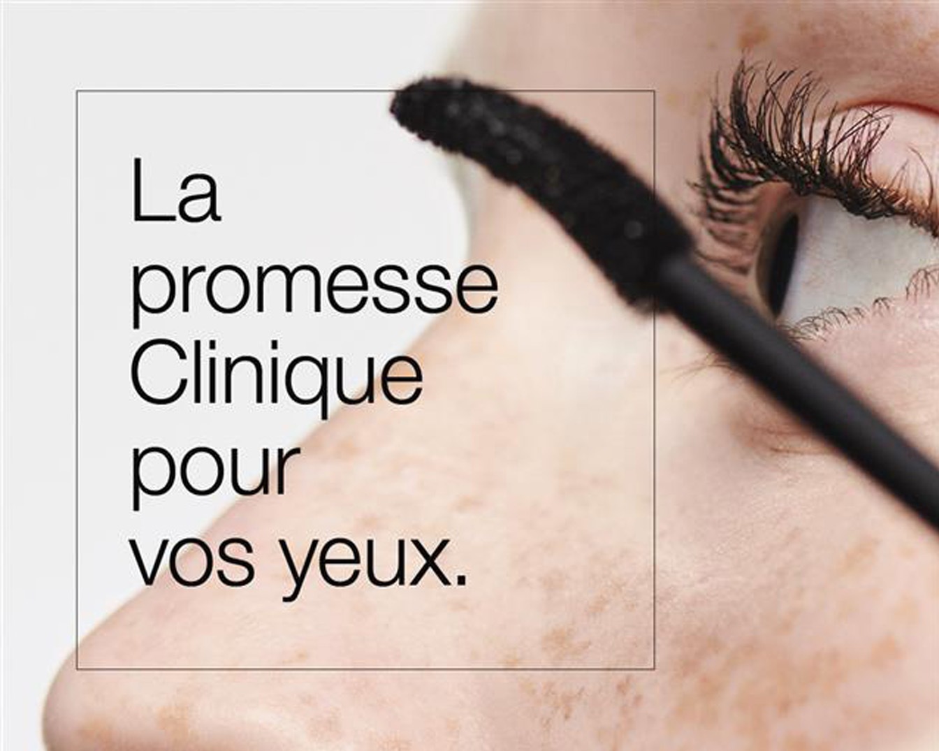 Gros plan sur un œil pendant qu’une personne applique du mascara noir sur ses cils. Le texte dans l’image indique: « La promesse Clinique pour vos yeux ».