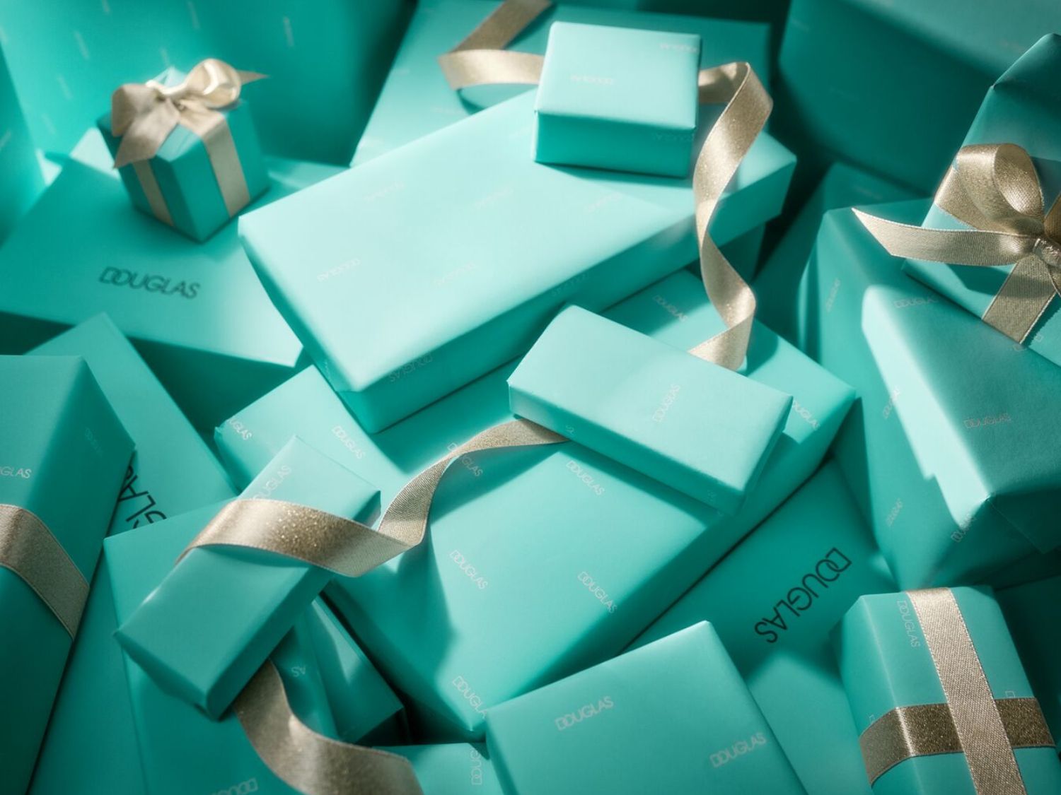 Een stapel turquoise Douglas-geschenkdozen, afgewerkt met glanzende gouden linten, klaar om uit te pakken en te genieten.