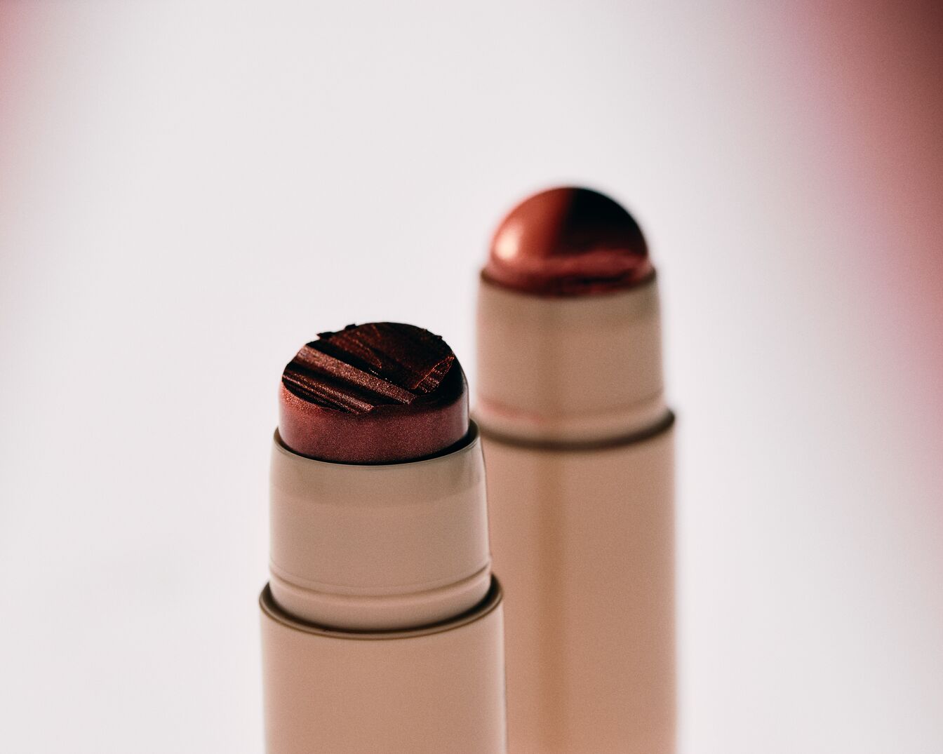 Nahaufnahme von zwei Make-up-Sticks mit cremiger, dunkelroter Textur in beigen Verpackungen.