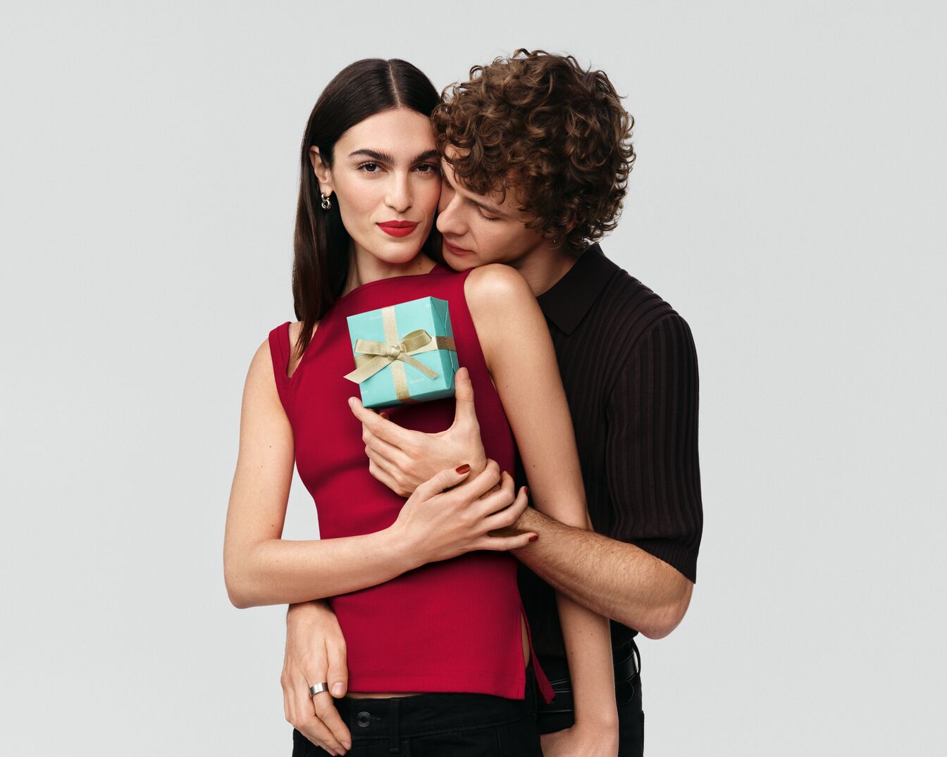 Ein Paar umarmt sich, die Frau hält eine kleine, hellblaue Geschenkbox mit einer goldenen Schleife, die ein Gefühl von Zuneigung und Wertschätzung vermittelt.