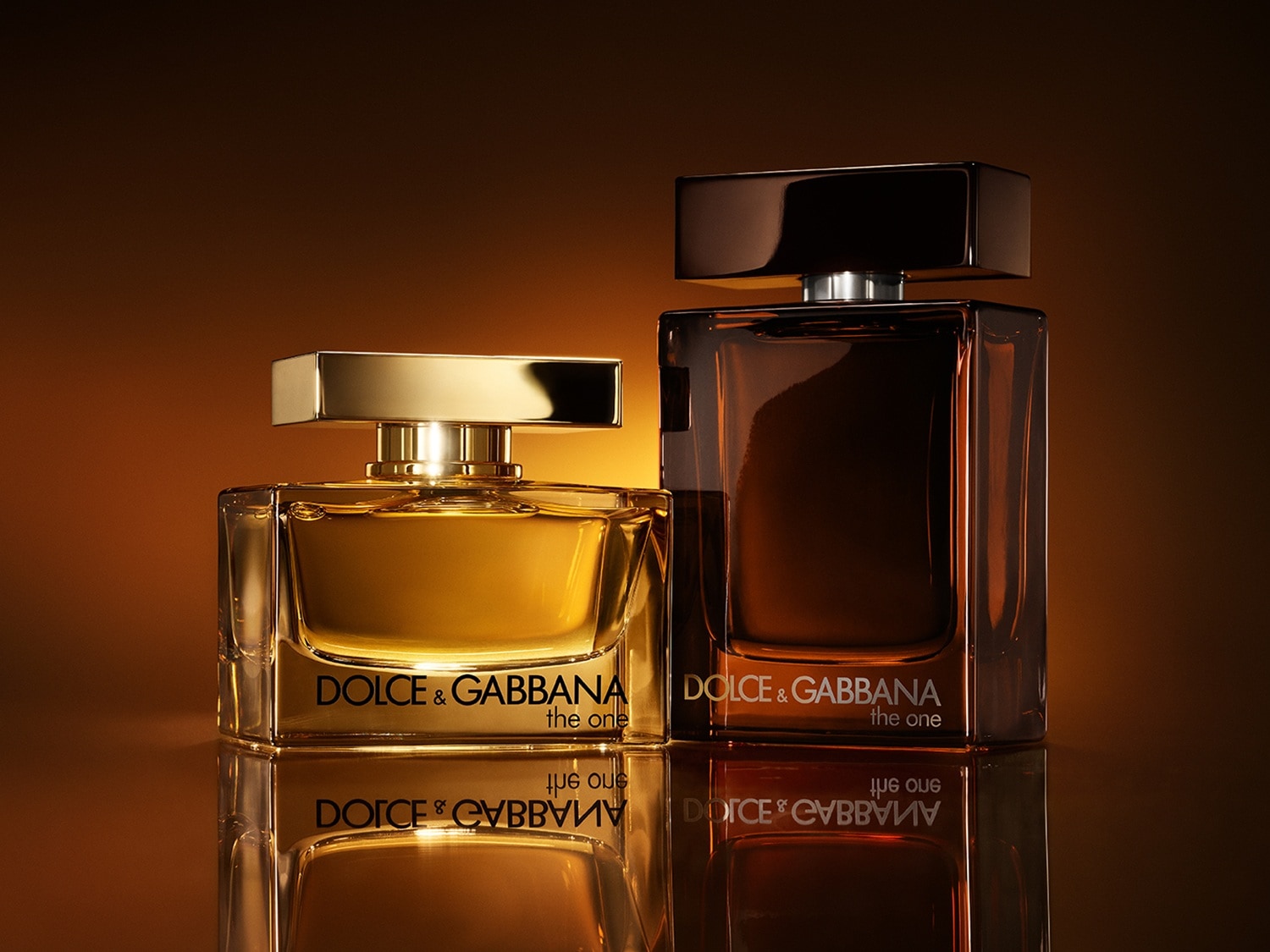 Zwei „The One"-Düfte von Dolce&Gabbana, der eine goldfarben und der andere in einem braunen Glasflakon, stehen auf einer glänzenden Oberfläche.