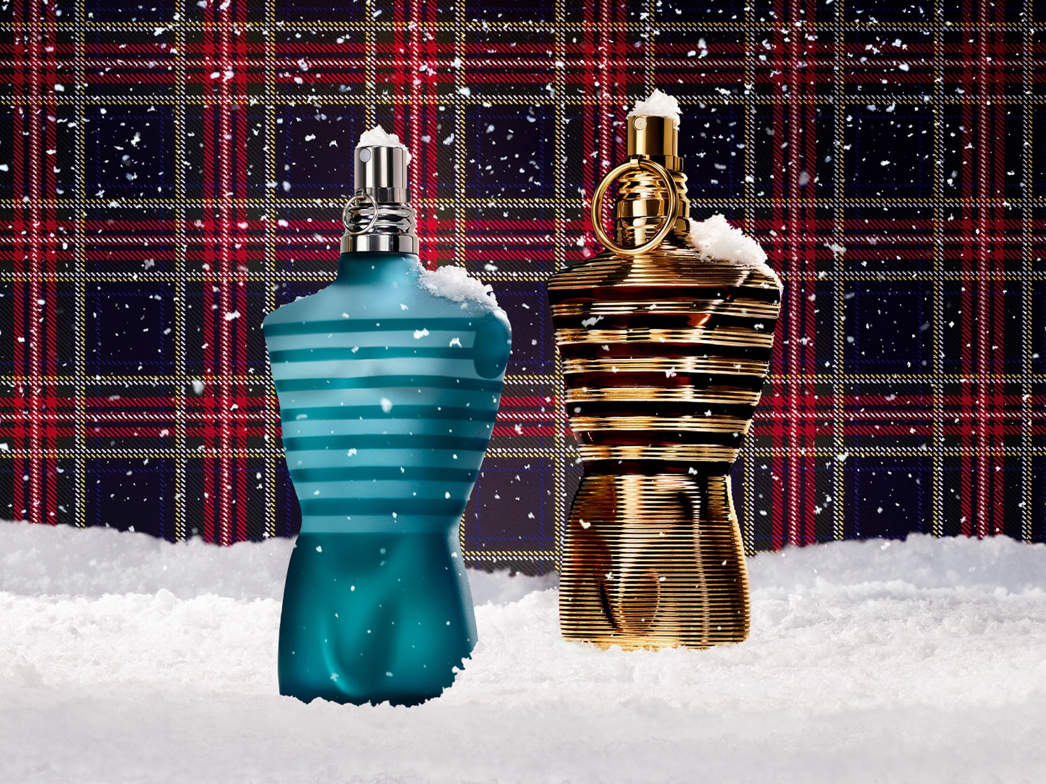 Dva flakony pánských parfémů ve tvaru mužského torza, jeden modrozelený s bílými pruhy a druhý zlatý s tmavými pruhy, oba zasněžené, na pozadí kostkované látky.