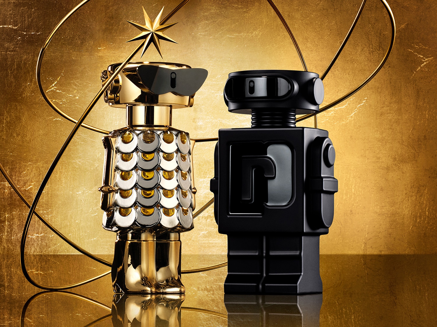 Dva flakony parfému ve tvaru robota, jeden zlatý s ozdobami a slunečními brýlemi, druhý černý s logem, na zlatém pozadí.