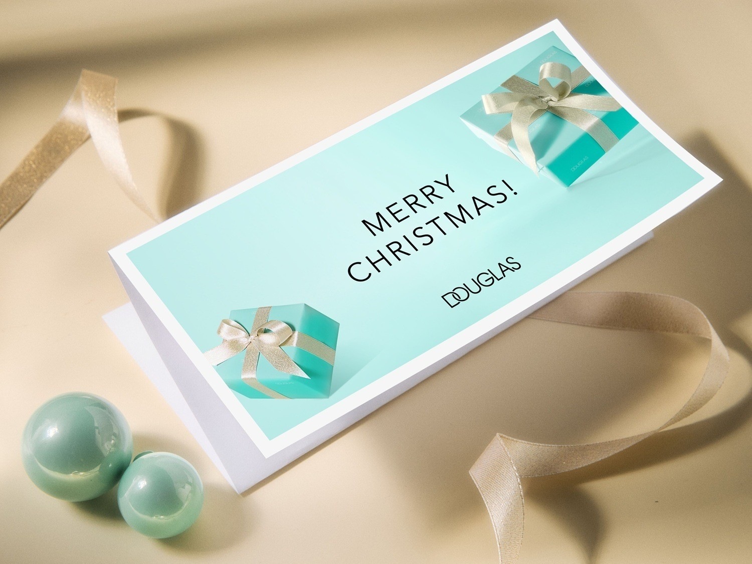 Festliche Douglas Grußkarte mit der Aufschrift 'Merry Christmas!' und einer Illustration von einem Geschenk, umgeben von schimmernden Kugeln und einem goldenen Band.