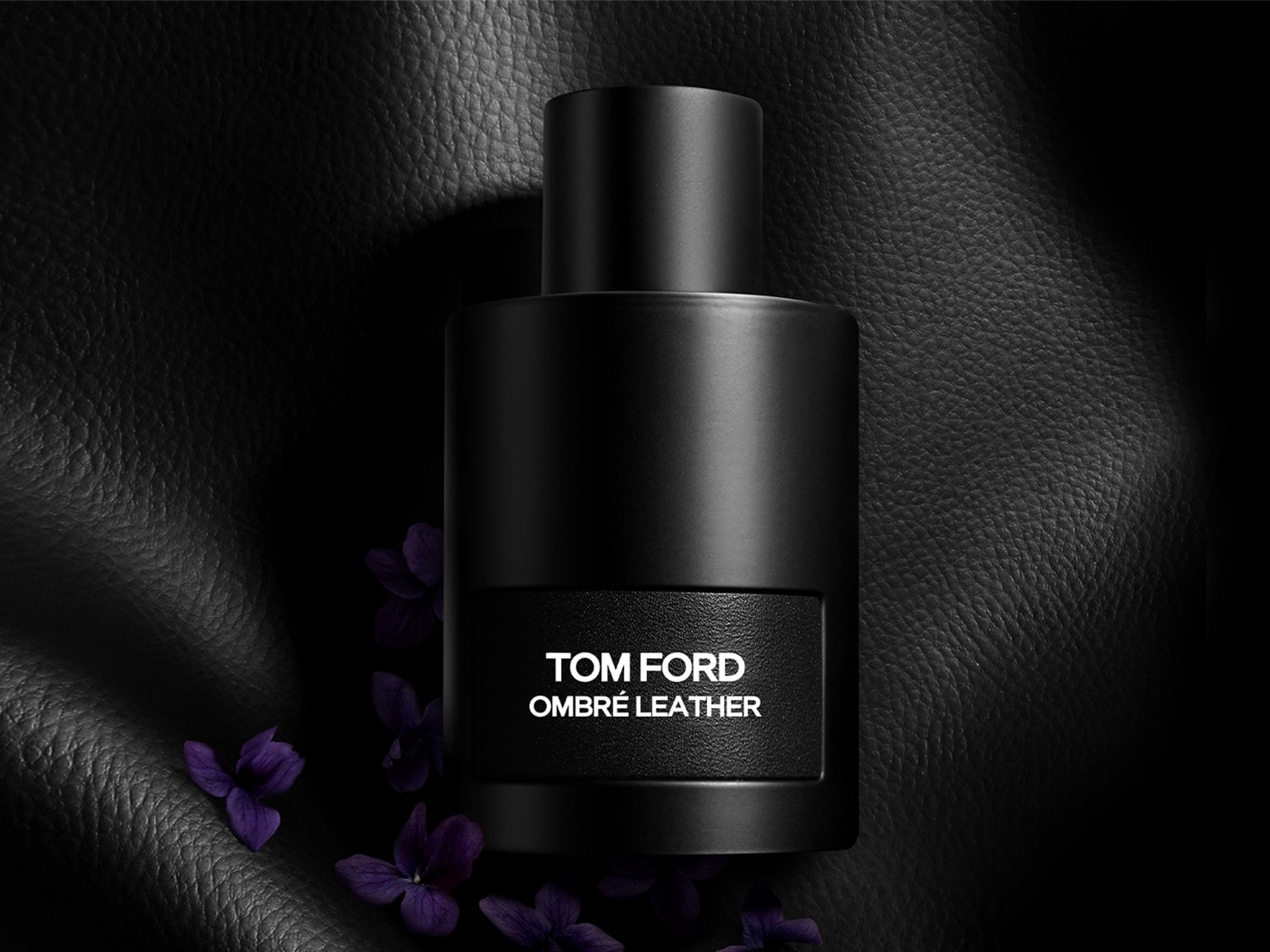 Le parfum Tom Ford Ombré Leather dans un flacon noir élégant, rehaussé de délicates fleurs violettes, évoquant un luxe raffiné et une senteur captivante.