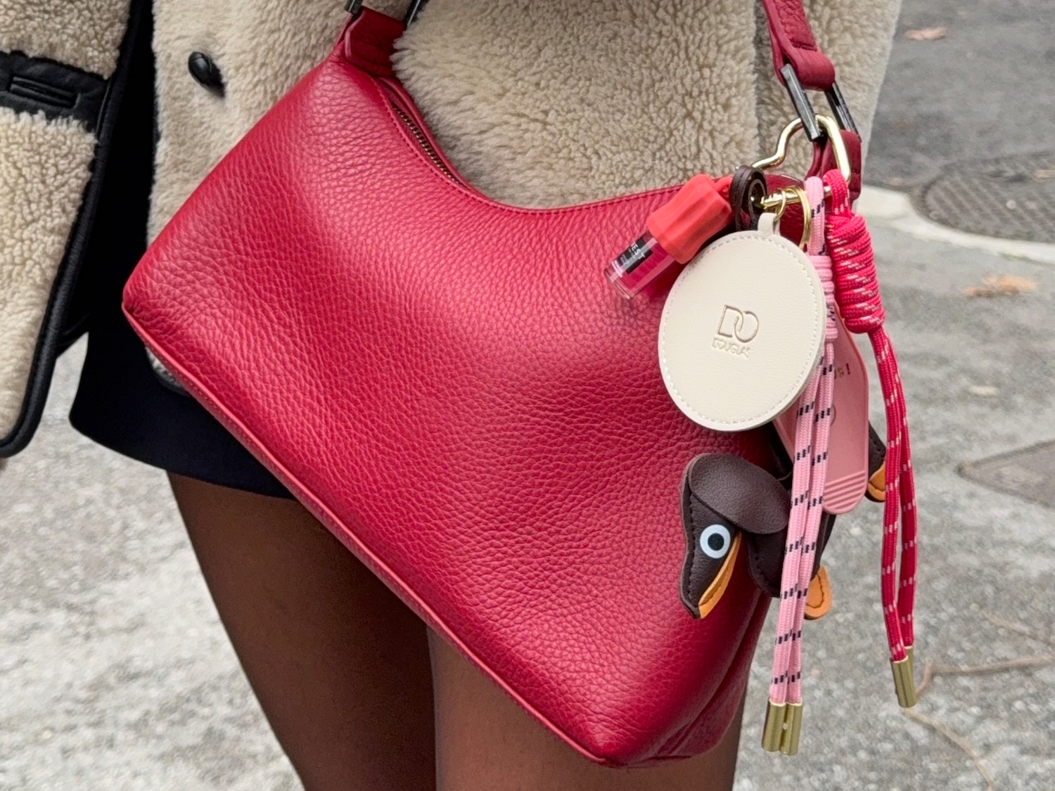 Nahaufnahme einer roten Handtasche mit verschiedenen Anhängern, darunter ein Douglas-Logo, die an einer Person hängt.