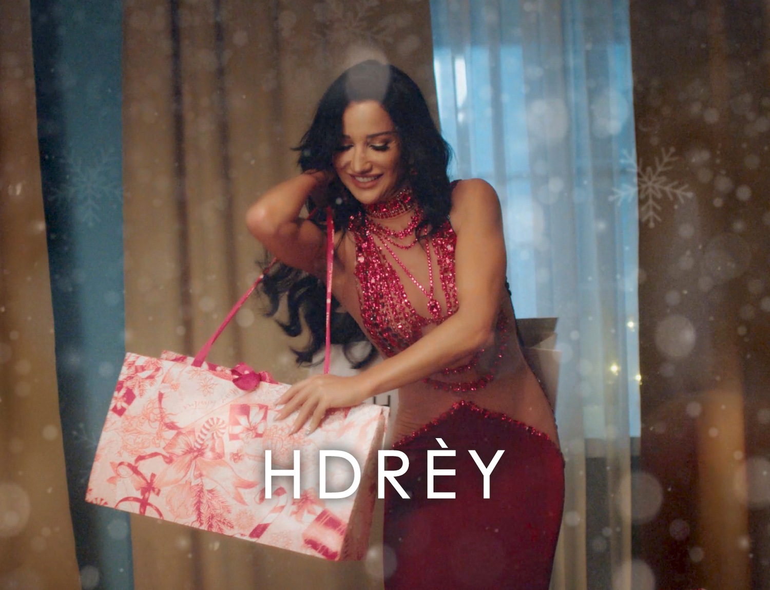 Uśmiechnięta kobieta w czerwonej sukience trzyma torbę na zakupy marki HDRÈY, idealną na świąteczne prezenty.