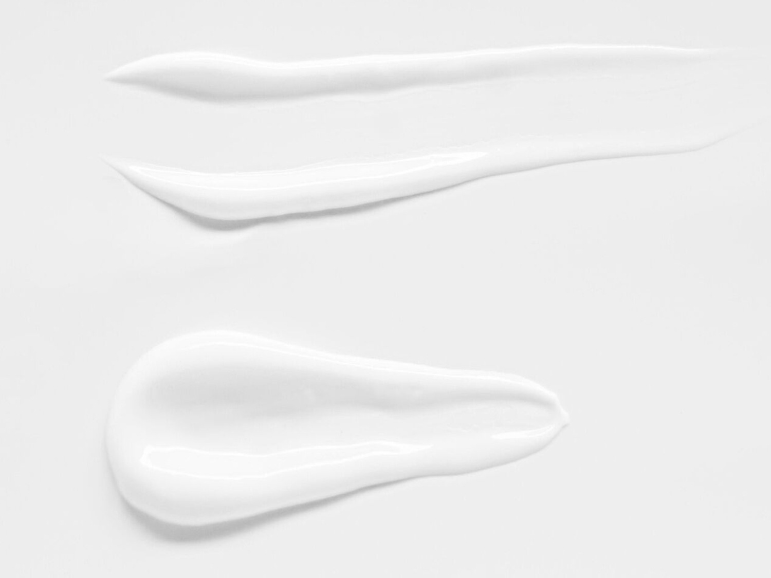 Baltos spalvos kremo tekstūros tepinėliai ant balto fono, demonstruojantys kremo švelnumą ir drėkinimą.