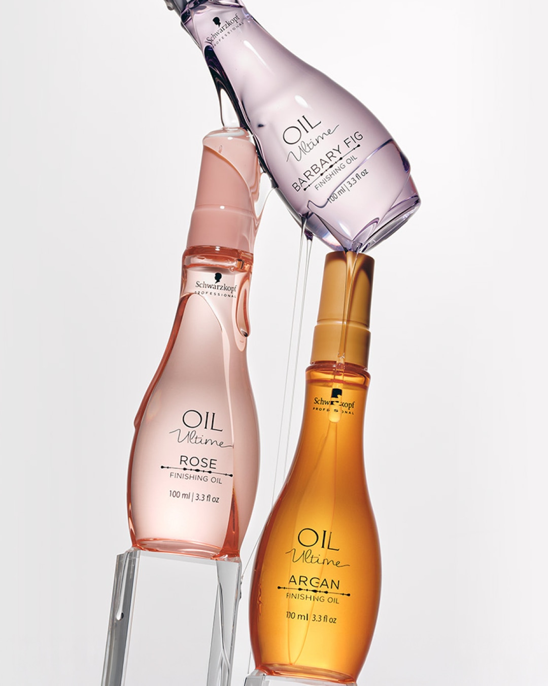 Trzy butelki olejku do włosów Schwarzkopf Oil Ultime: fioletowa Barbary Fig, różowa Rose i pomarańczowa Argan, każda o pojemności 100 ml.