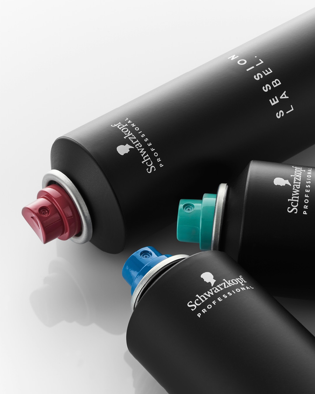 Trzy czarne butelki lakieru do włosów Schwarzkopf Professional z rozpylaczami w kolorze czerwonym, turkusowym i niebieskim.