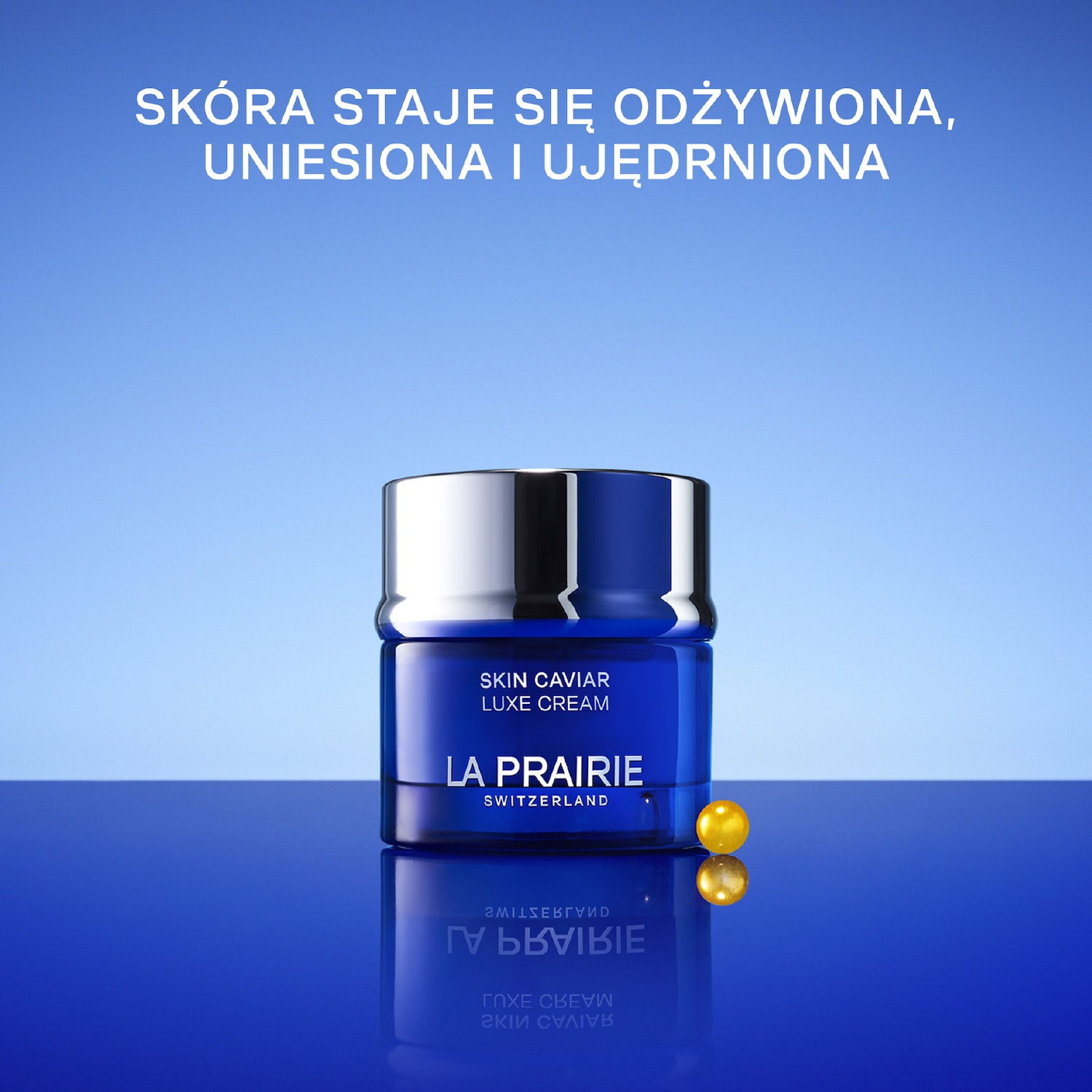 Niebieski słoiczek kremu La Prairie Skin Caviar Luxe Cream z srebrną nakrętką stoi na błyszczącym niebieskim tle, obok niego leży złota kulka. Skóra staje się odżywiona, uniesiona i ujędrniona.