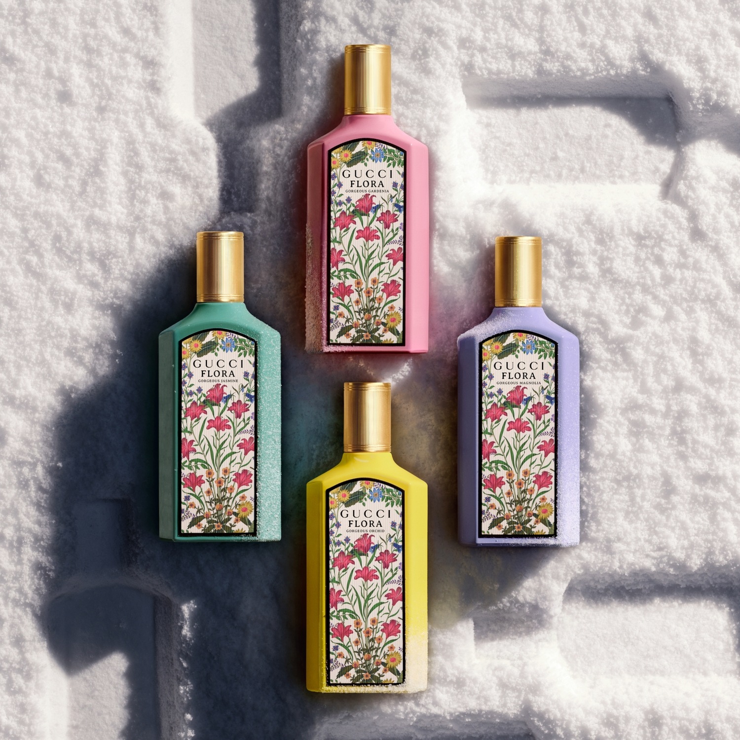 Vier kleurrijke Gucci Flora-parfums, waaronder Gardenia, Magnolia, Orchidee en Jasmijn, staan op een witte, besneeuwde achtergrond.
