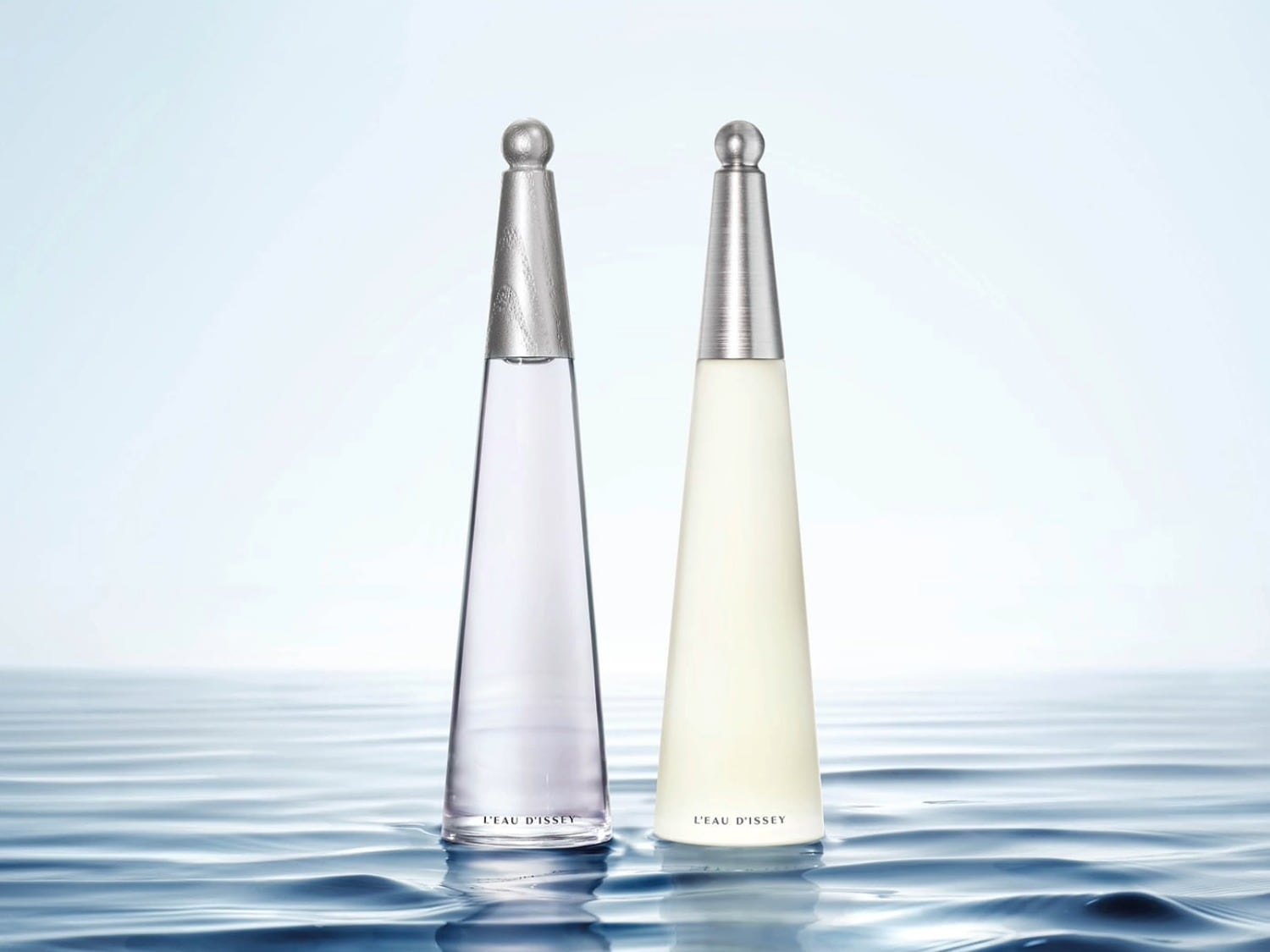 Twee L'Eau d'Issey-parfums staan op een wateroppervlak, de ene met een heldere, lila vloeistof en een zilveren dop, de andere met een crèmekleurige vloeistof en een zilveren dop.