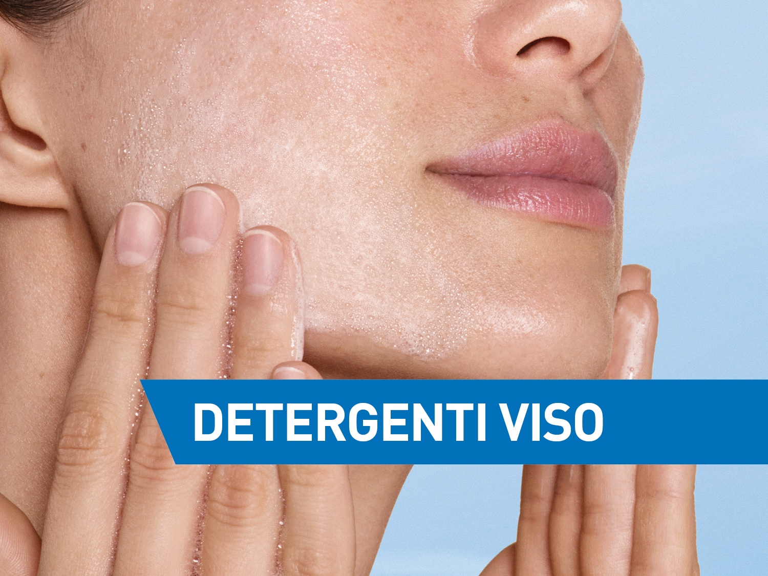 Primo piano di una donna che si deterge il viso con un detergente schiumogeno, con banner blu con la scritta 'Detergenti Viso'.