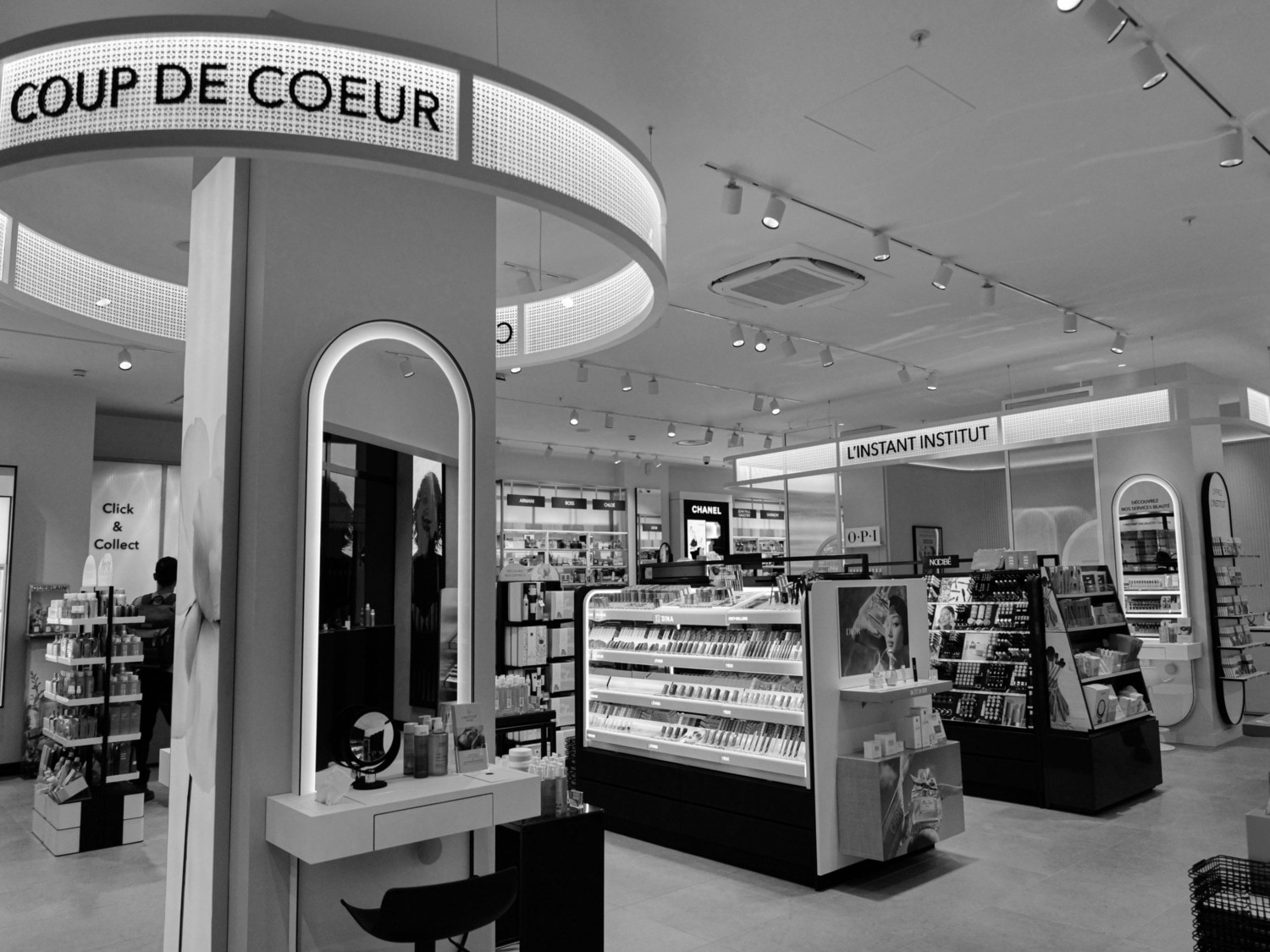 Découvrez l'intérieur d'un magasin de beauté, présentant des comptoirs de marques comme Chanel et O-P-I, sous un éclairage moderne et des enseignes élégantes.