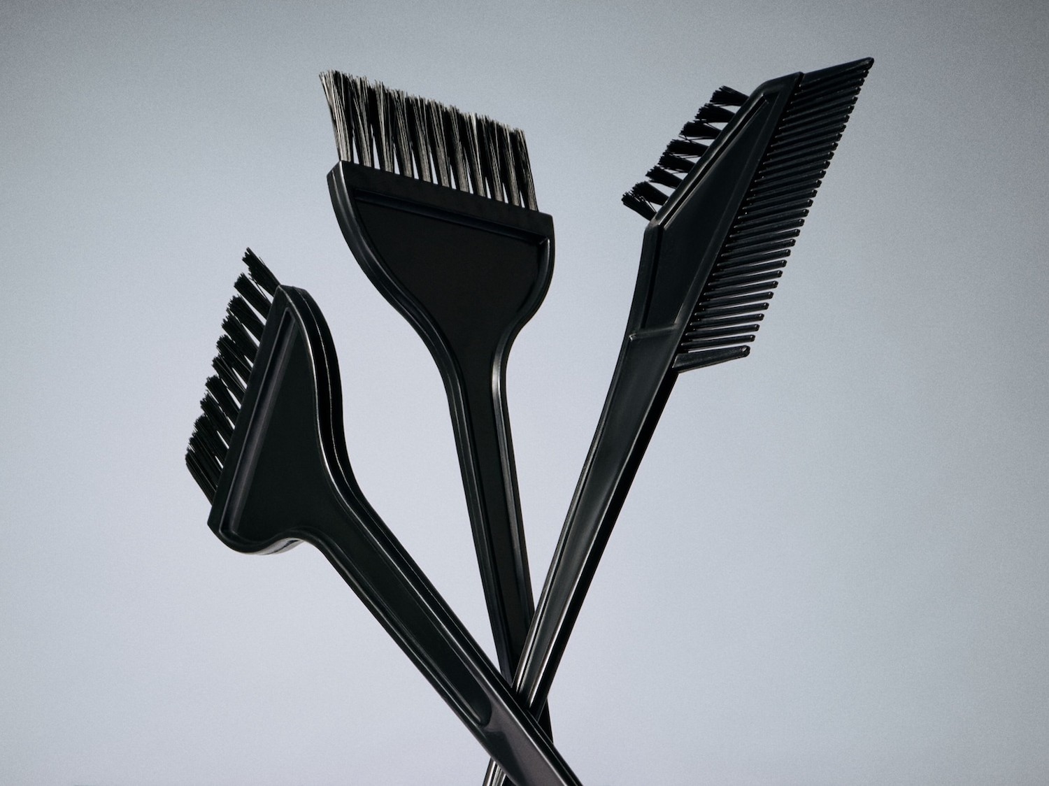 Drei schwarze Friseurbürsten und ein Kamm liegen übereinander und sind bereit für die Anwendung von Farbe oder Tönung.