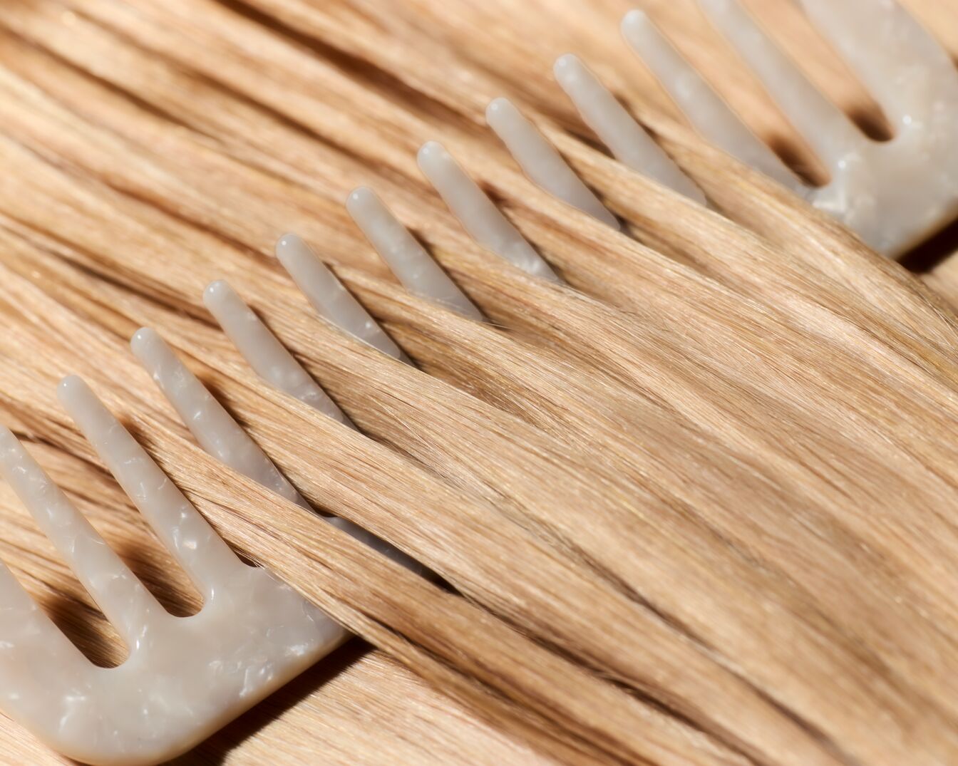 Nahaufnahme von blonden Haarsträhnen, die mit einem grauen Kamm gekämmt werden, um die Textur und Farbe des Haares hervorzuheben.