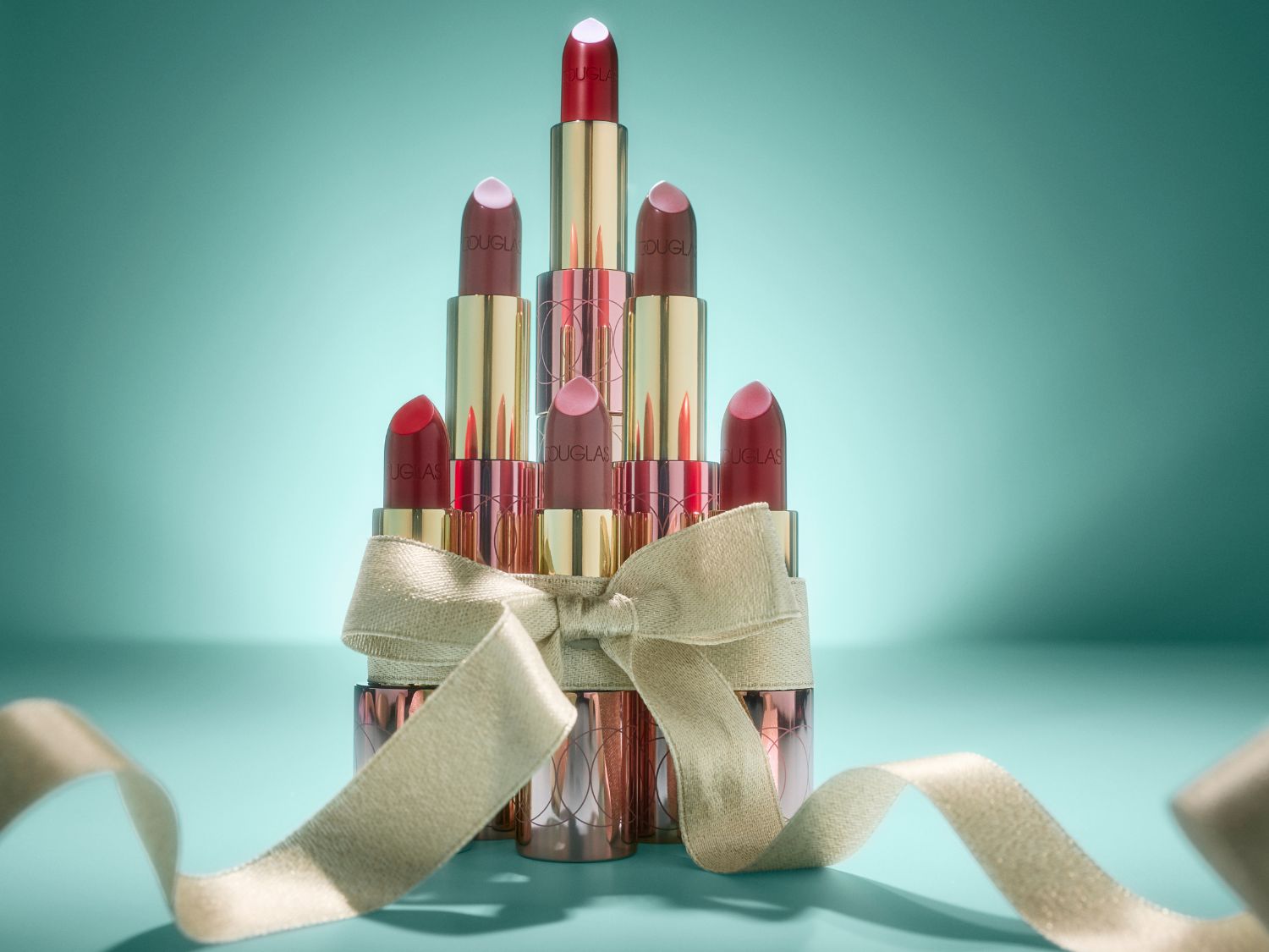Stapel Douglas-lippenstiften in verschillende tinten, vastgebonden met een gouden lint, tegen een blauwe achtergrond.