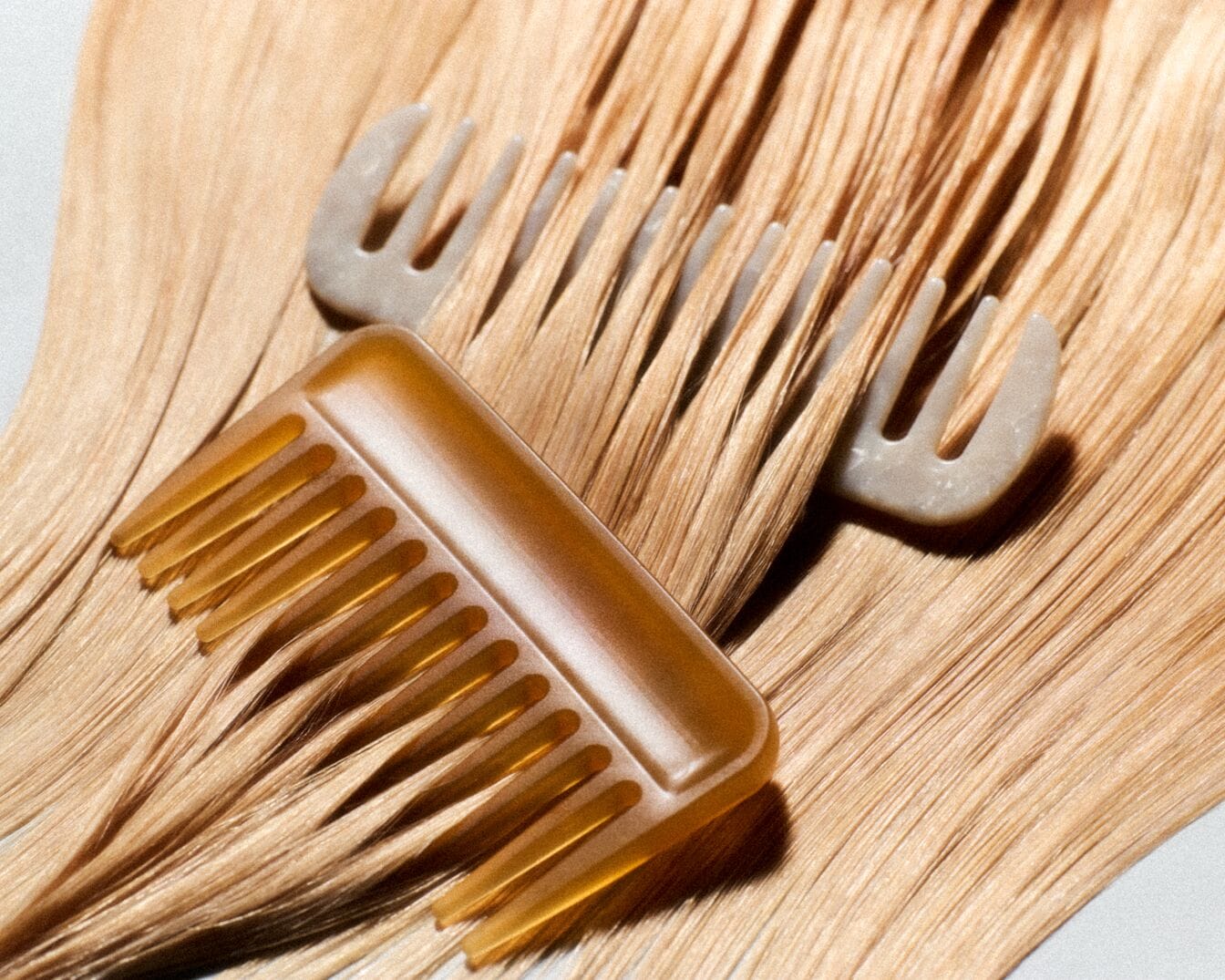 Dwa grzebienie leżą na blond włosach, jeden jest brązowy, a drugi szary.