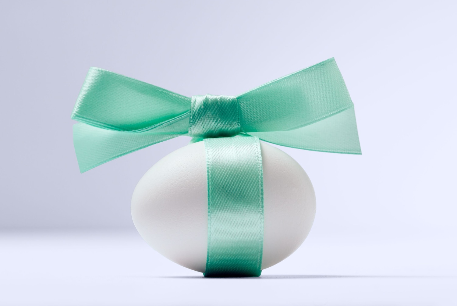 Ein weißes Ei ist mit einem hellgrünen Band und einer Schleife verziert, die eine festliche und elegante Note verleihen.