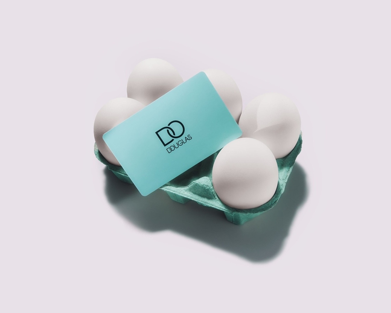 Šeši balti kiaušiniai žalioje dėžutėje su mėlyna Douglas dovanų kortele ant viršaus.
