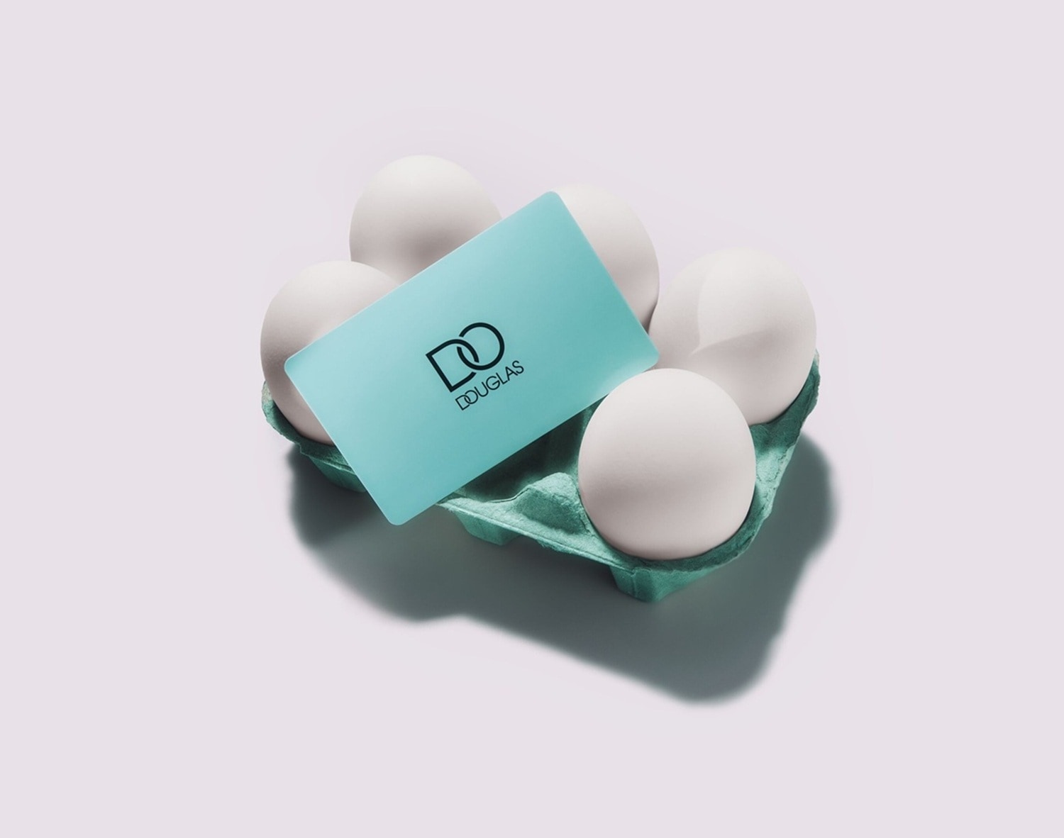Ein türkisfarbener Douglas-Gutschein liegt auf einer Eierpackung mit weißen Eiern.
