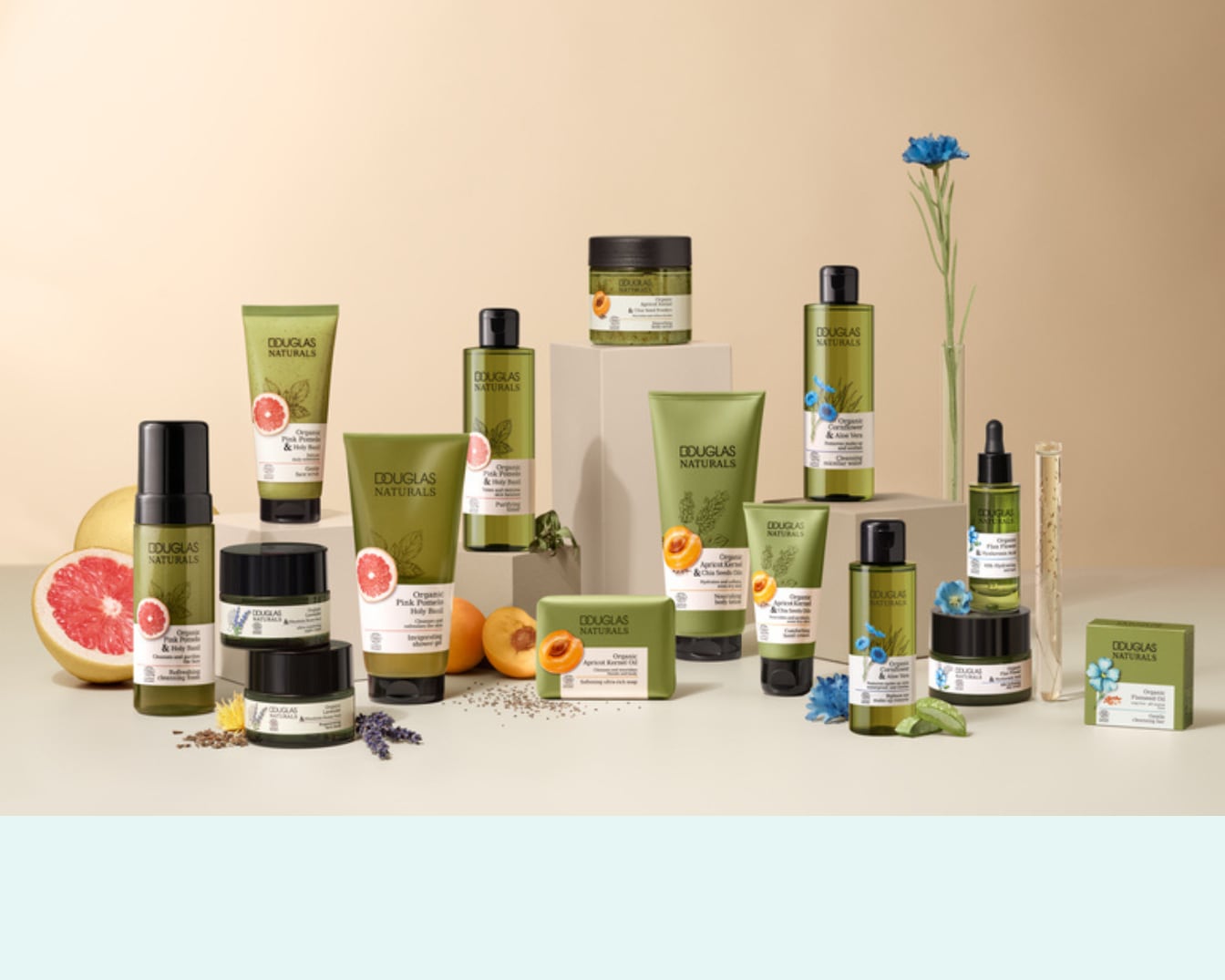 Een verzameling Douglas Naturals-producten, waaronder huidverzorging met roze pompelmoes en abrikozenpit, gepresenteerd met verse ingrediënten en bloemen.