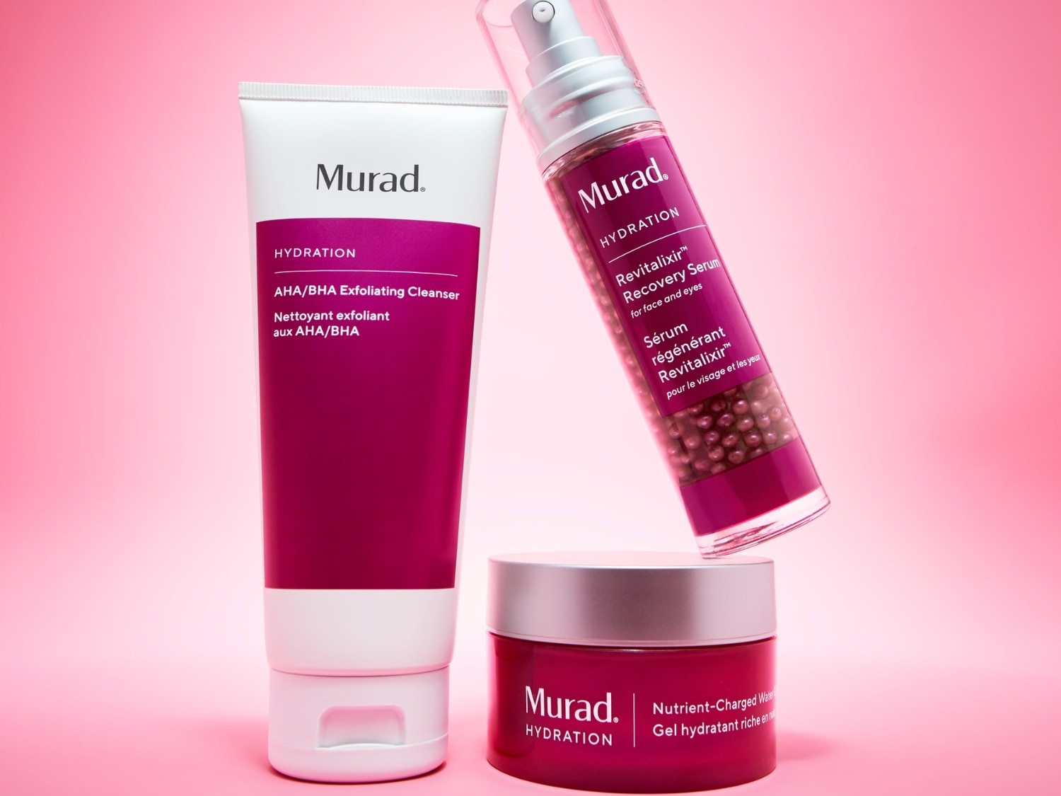 Trzy produkty Murad Hydration: peelingujący żel oczyszczający AHA/BHA w białej tubie z fuksjowym paskiem, serum Revitalixir Recovery w przezroczystej butelce z fuksjową etykietą i żel nawilżający Nutrient-Charged Water w fuksjowym słoiczku.