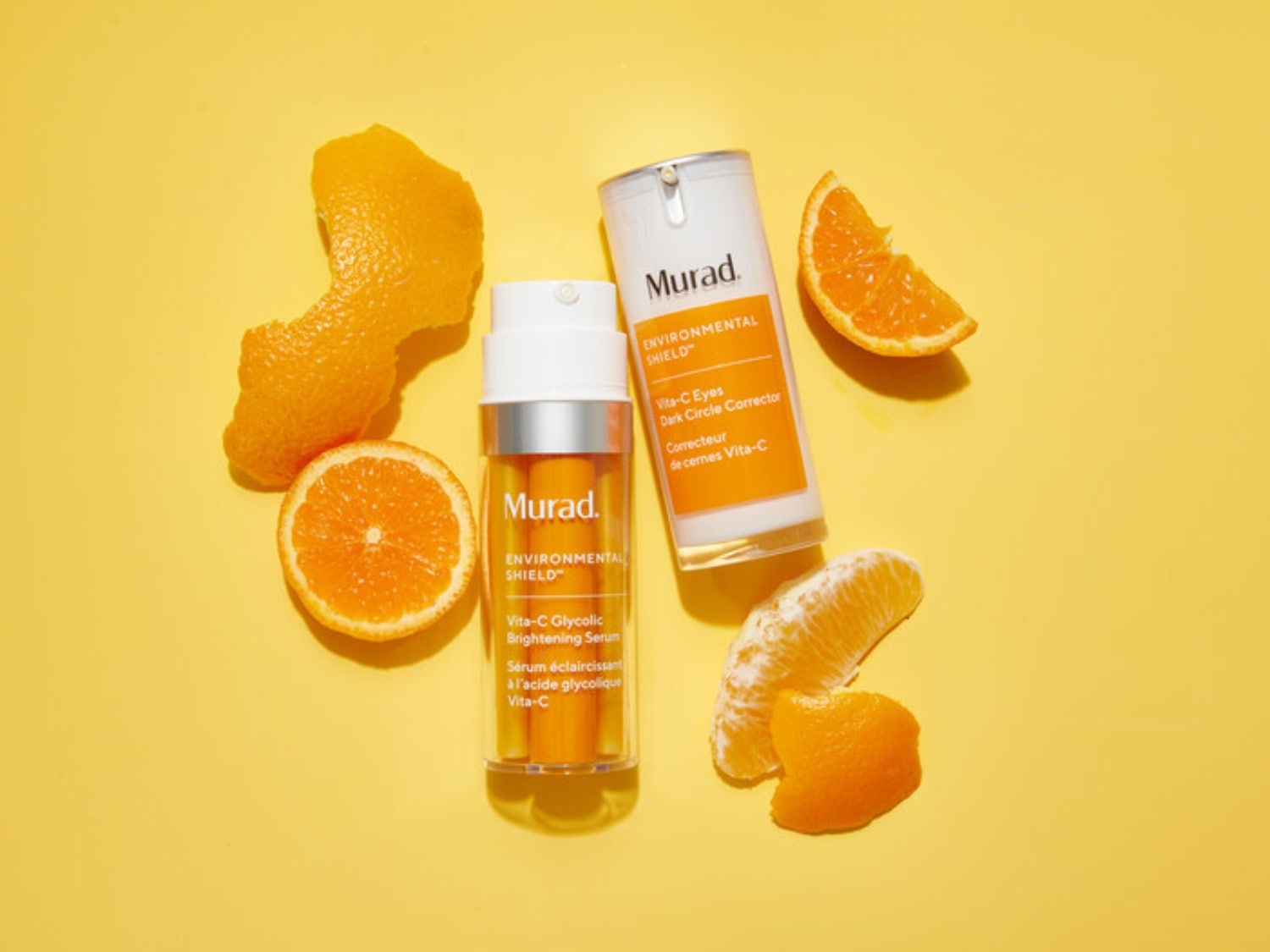 Dwa produkty Murad z serii Environmental Shield Vita-C, serum rozjaśniające i korektor na cienie pod oczami, otoczone pomarańczami na żółtym tle.