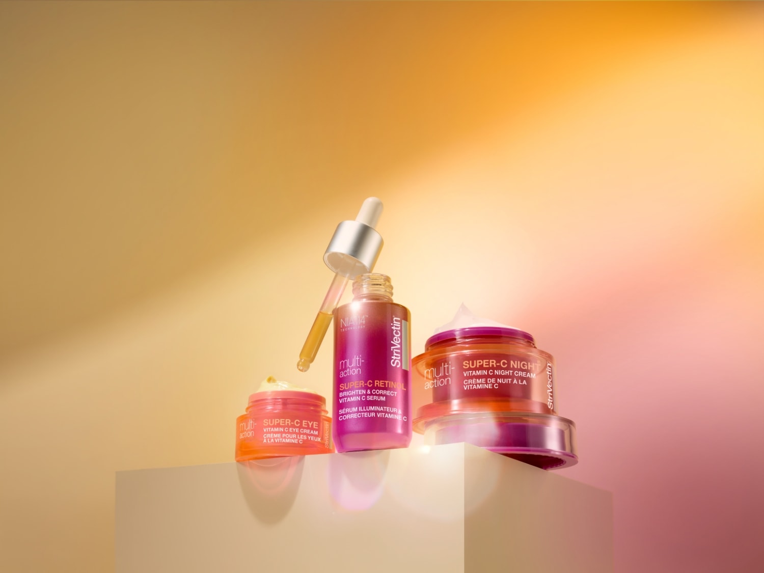Na beżowym tle znajdują się trzy produkty StriVectin: krem pod oczy Super-C w pomarańczowym opakowaniu, serum Super-C Retinol w różowym opakowaniu z pipetą oraz krem na noc Super-C w różowym słoiczku.