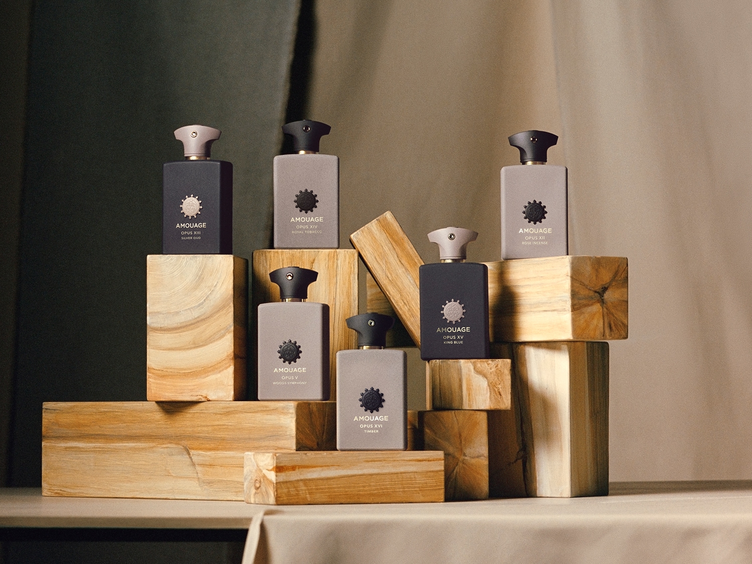 Eine Auswahl an Amouage Parfums, darunter Opus XIII Silver Oud, Opus XIV Royal Tobacco, Opus V Woods Symphony, Opus XVI Timber, Opus XV King Blue und Opus XII Rose Incense, kunstvoll auf Holzblöcken arrangiert.