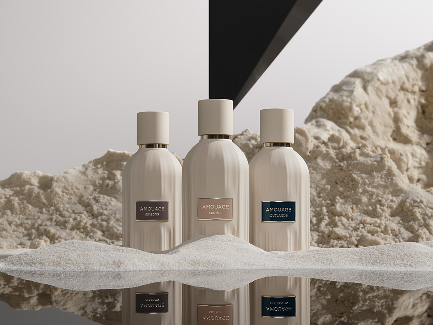 Drei Amouage-Parfümflaschen in Weißtönen stehen auf Sand, wobei die Namen Reasons, Lustre und Outlands auf den Etiketten stehen.