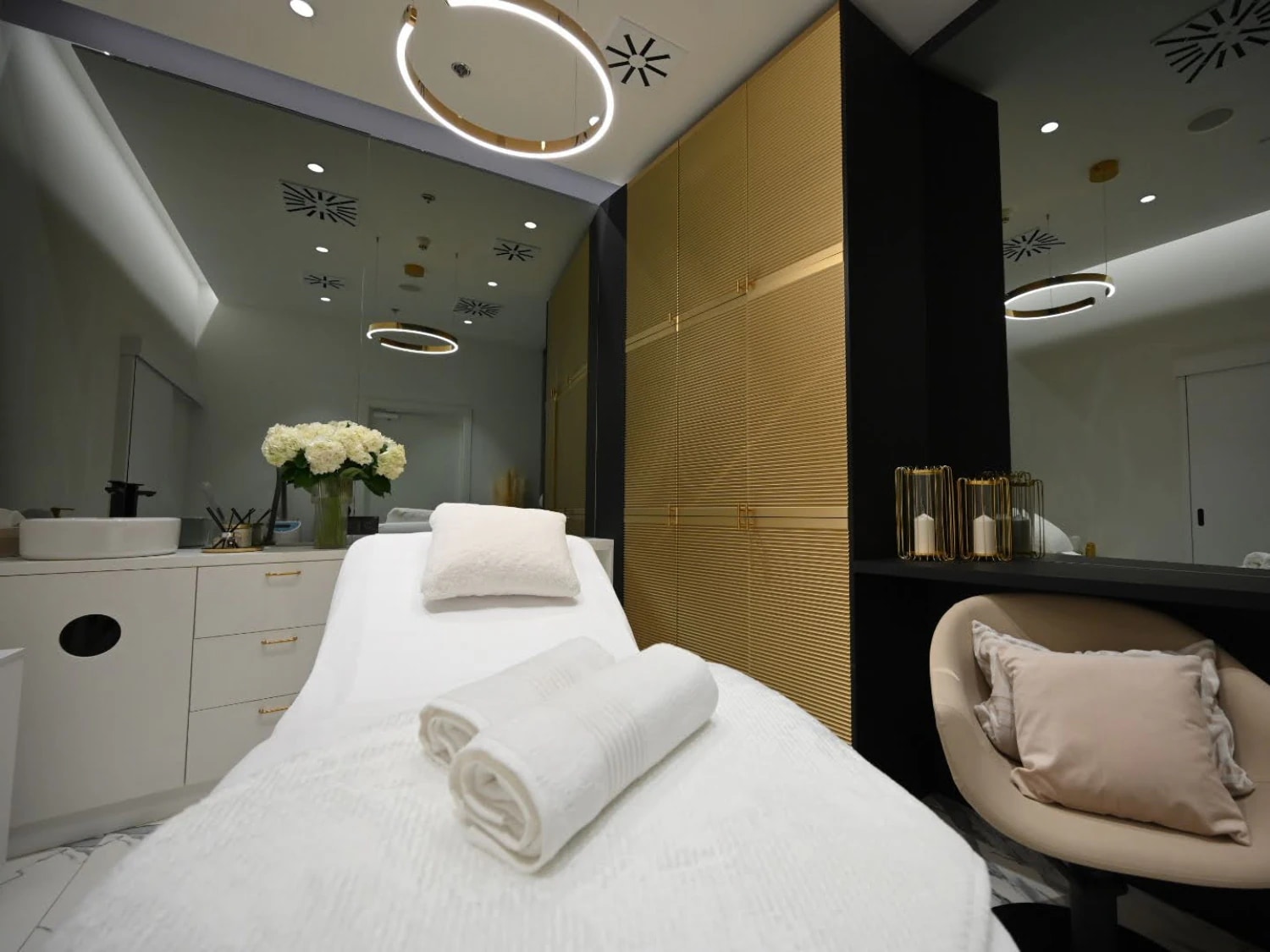 Jasne wnętrze salonu spa z białym łóżkiem do masażu, miękkimi ręcznikami i dekoracyjnymi elementami, tworzące relaksującą atmosferę.