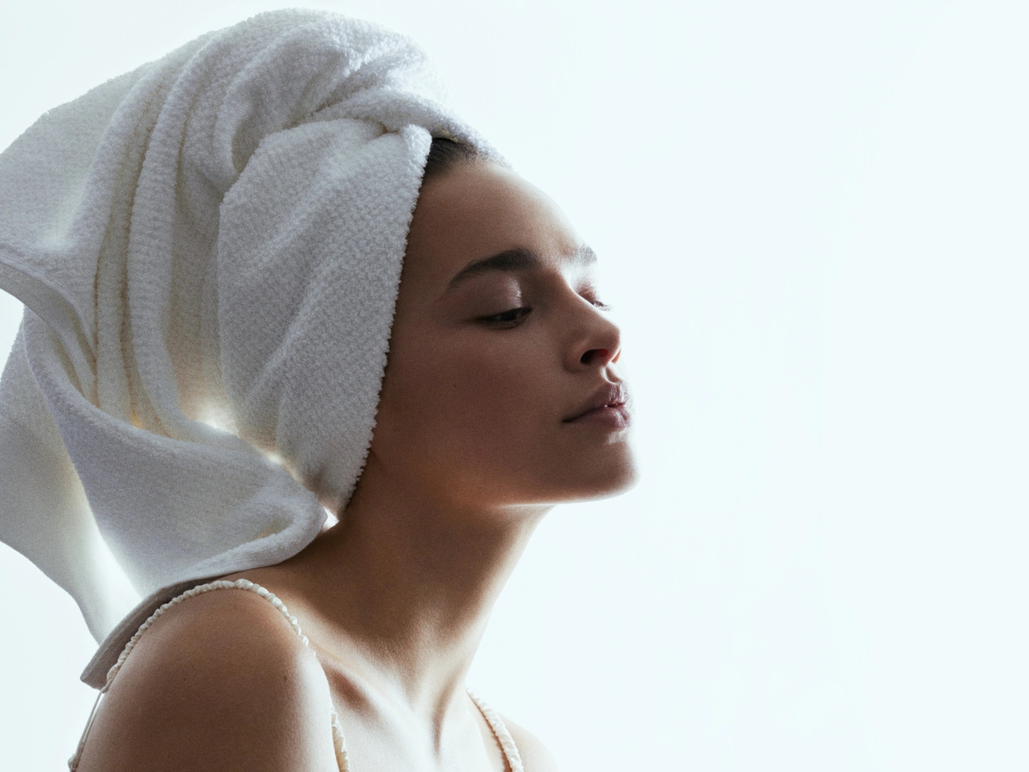 Profil kobiety z białym ręcznikiem na głowie, skóra jest gładka i promienna, co sugeruje pielęgnację.