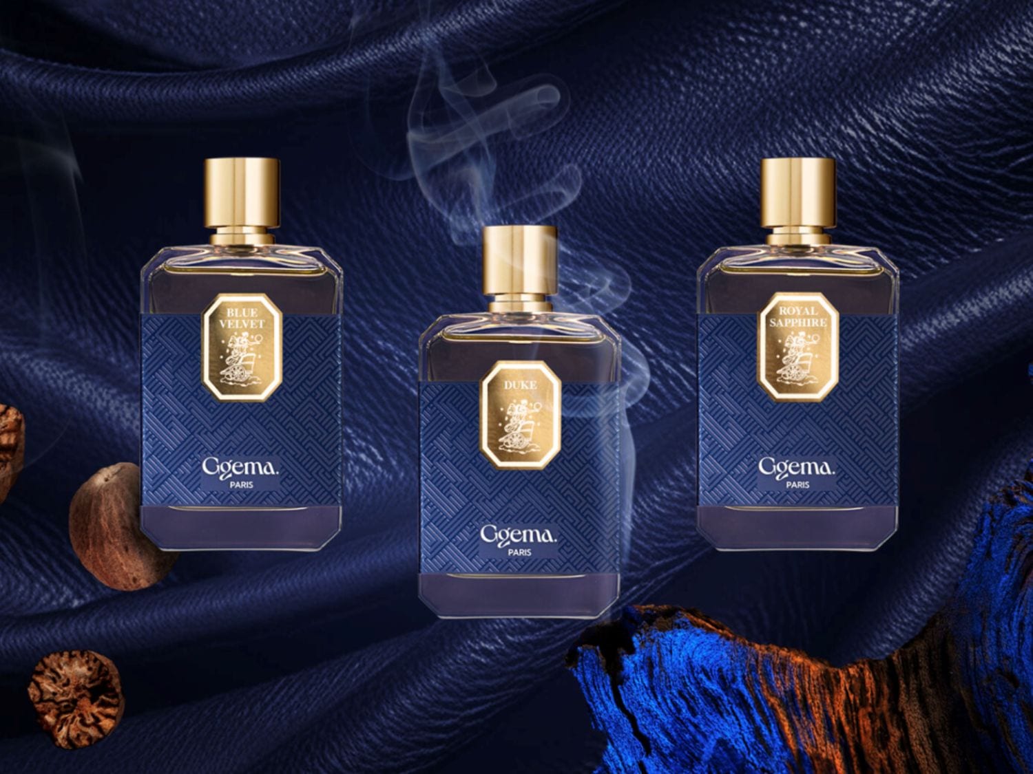 Trzy flakony perfum Cgema Paris: Blue Velvet, Duke i Royal Sapphire, każdy z złotą nakrętką i etykietą na tle granatowej tkaniny.
