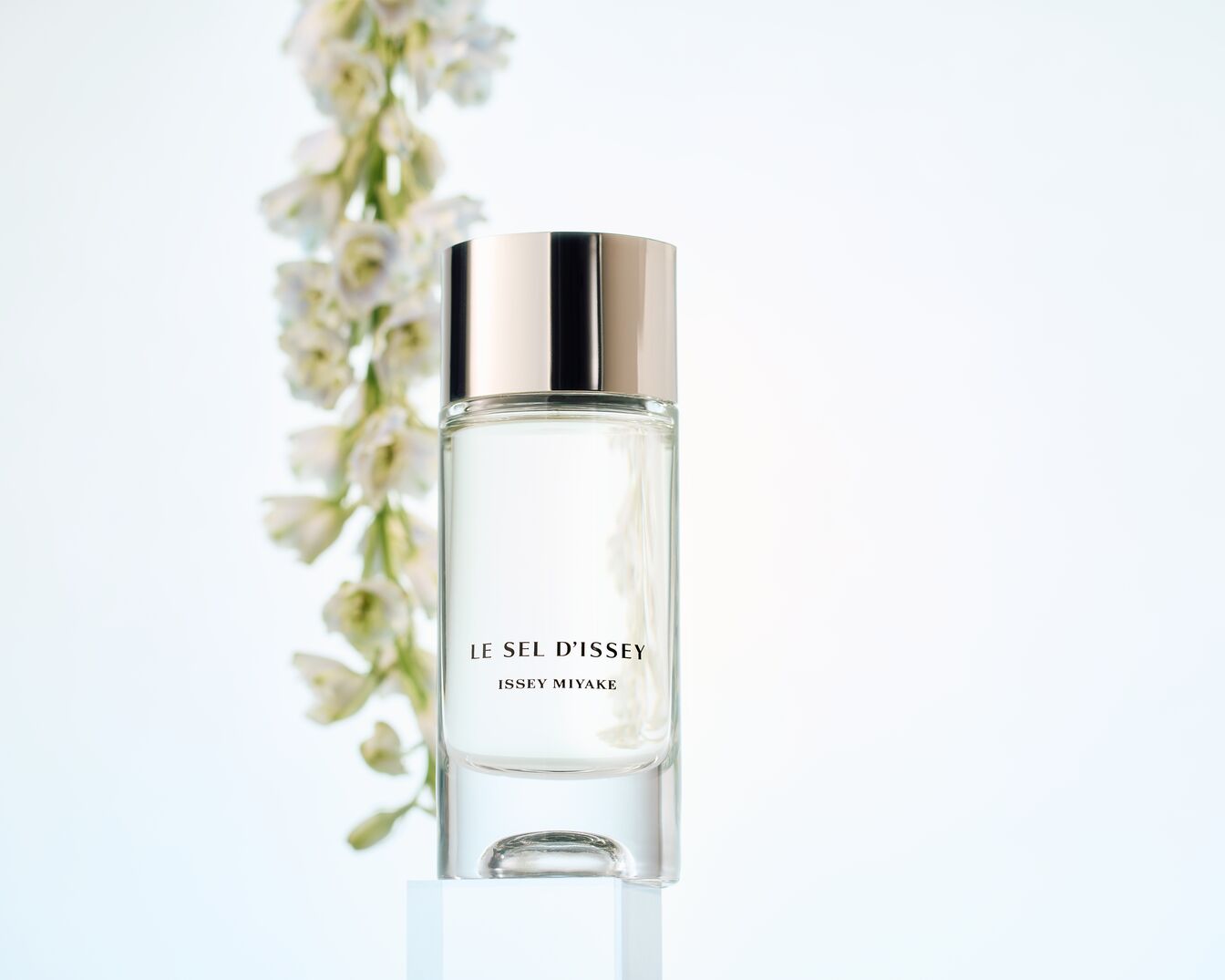 Eine durchsichtige Flasche Le Sel d'Issey Issey Miyake Eau de Parfum steht neben einem weißen Blütenzweig.