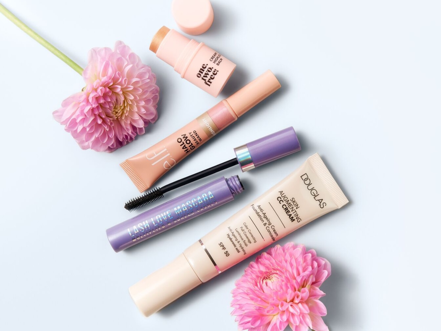 Entdecke eine Auswahl an Make-up-Produkten, darunter Douglas CC Cream, e.l.f. Halo Glow Beauty Wand, One.Two.Free! Cream Highlight Balm und Lash Love Mascara, kunstvoll arrangiert mit rosa Blumen.