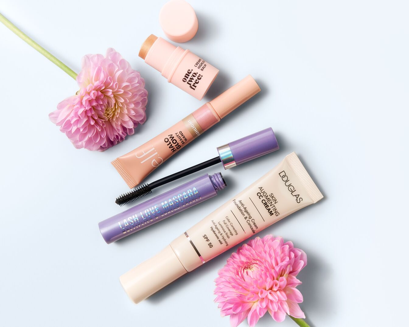 Entdecke eine Auswahl an Make-up-Produkten, darunter Douglas CC Cream, e.l.f. Halo Glow Beauty Wand und Lash Love Mascara, kunstvoll arrangiert mit rosa Dahlienblüten.