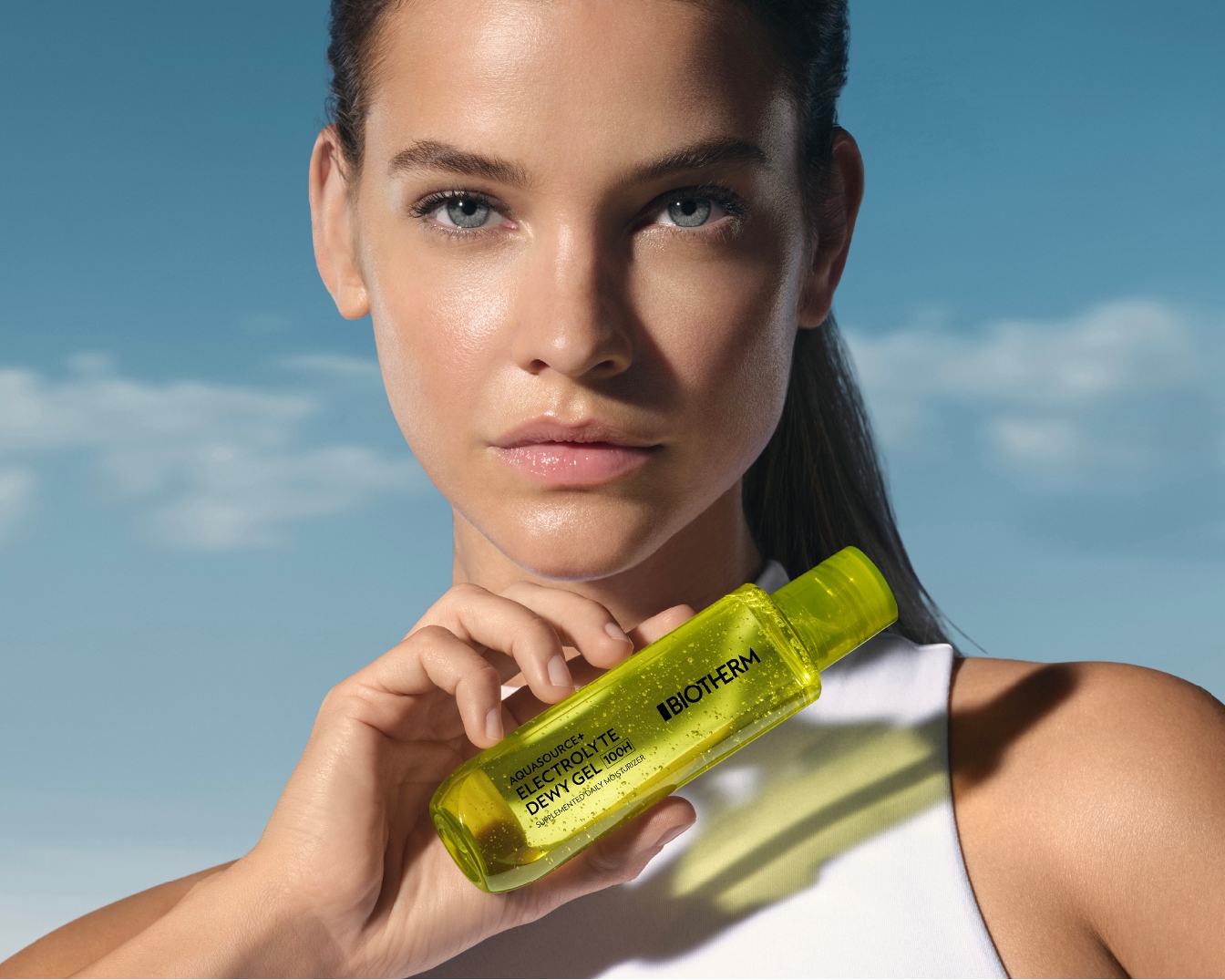 Une femme tient un gel hydratant Biotherm Aquasource+ Electrolyte Dewy Gel 100H dans un flacon vert transparent.