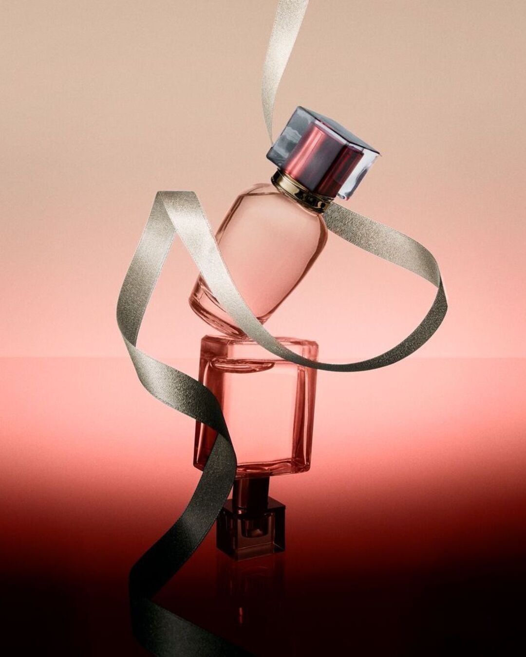 Deux flacons de parfum roses empilés, entourés d'un ruban argenté, évoquant l'élégance et le luxe.