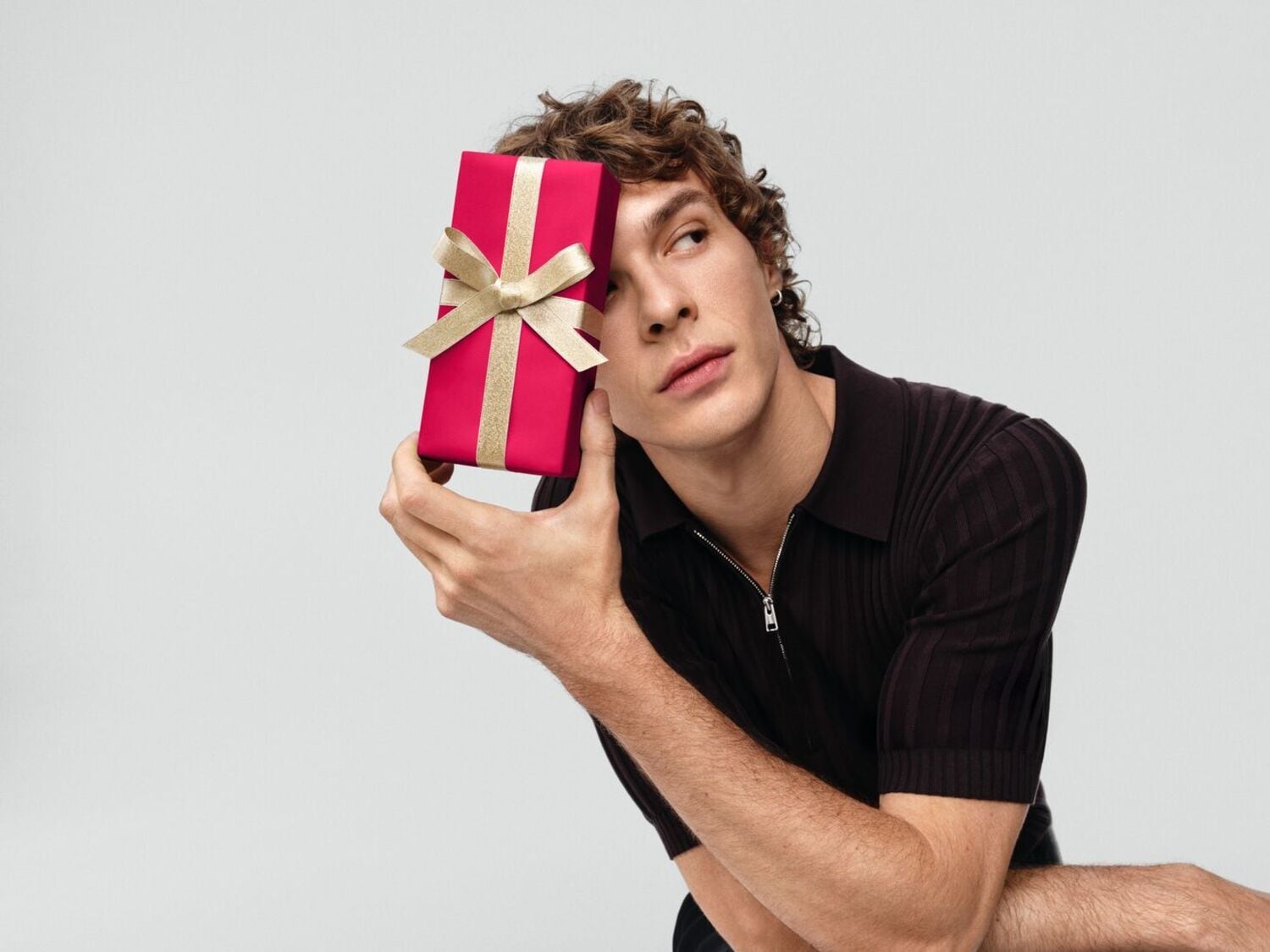 Un homme tient un cadeau rouge avec un ruban doré, ajoutant une touche de mystère et d'excitation.