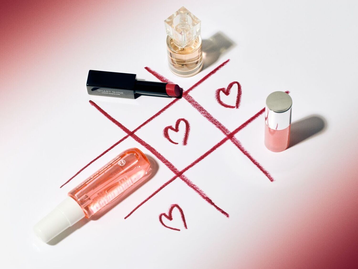 Découvrez une collection de produits de beauté disposés sur un jeu de morpion dessiné avec des coeurs, comprenant un rouge à lèvres noir Smart Shine, un parfum et un brillant à lèvres rose.