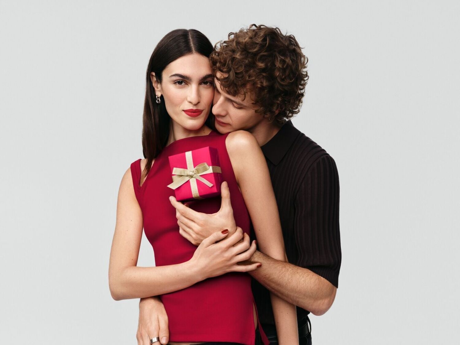 Un couple enlacé, la femme tenant un petit cadeau rouge orné d'un ruban doré, symbole d'affection et de partage.