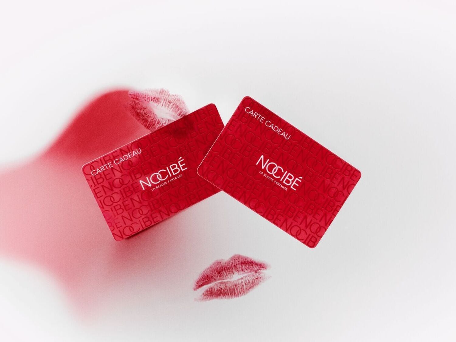 Deux cartes cadeaux rouges Nocibé sont présentées avec des motifs de rouge à lèvres, offrant une idée cadeau beauté idéale.