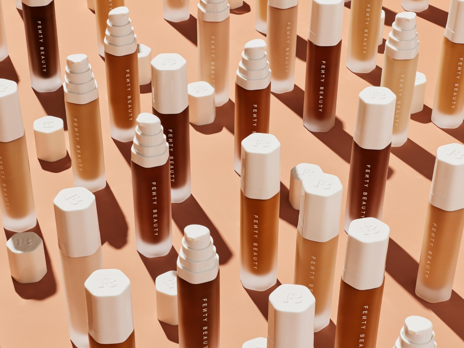 Découvrez une gamme de fonds de teint Fenty Beauty dans diverses nuances, présentés dans des flacons élégants avec des bouchons blancs.